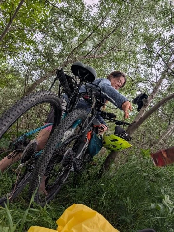 A fully loaded touring bike leaned into dense green brush while Skizzi sets up a wild camp among the trees