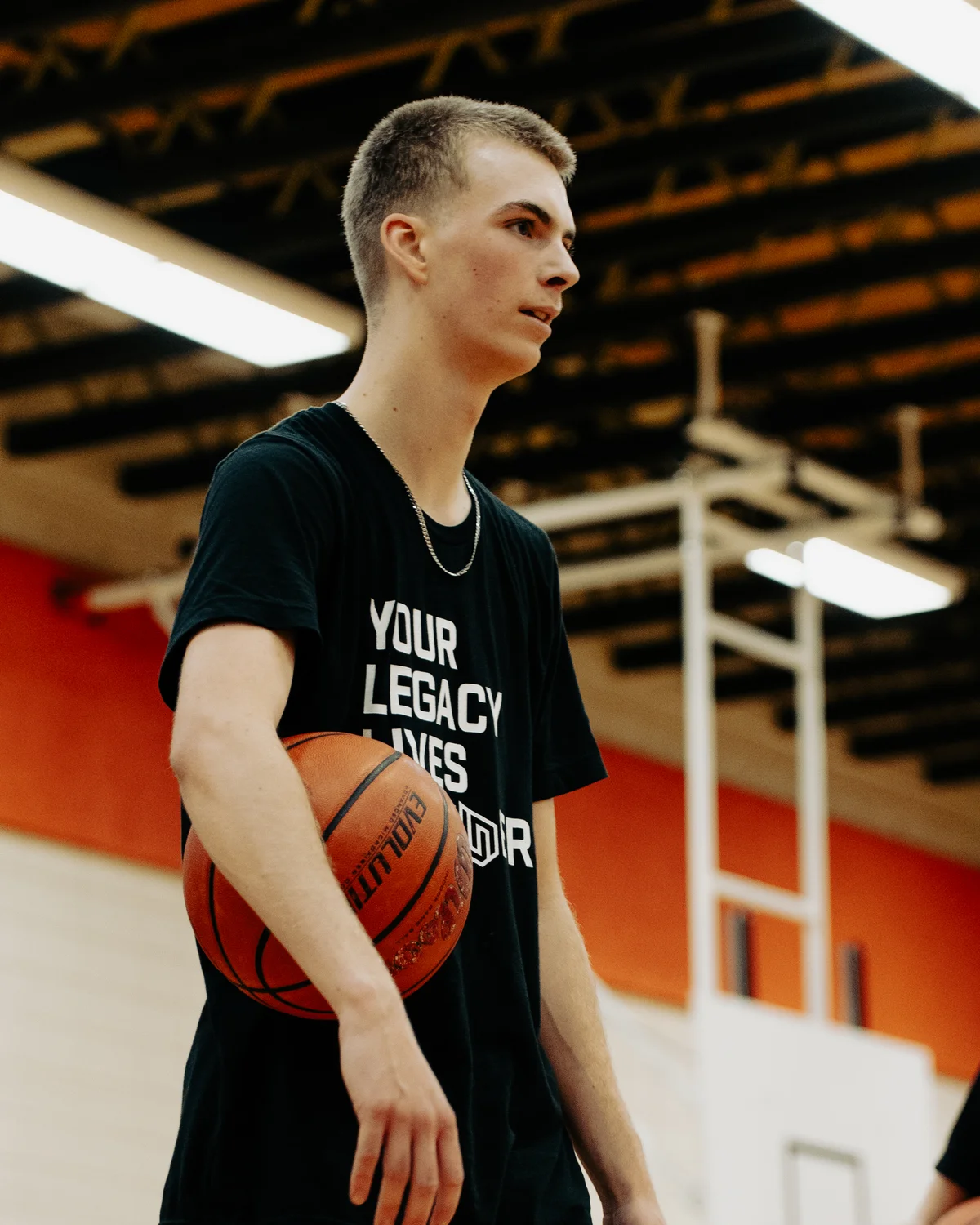 Baron Schultz holding a basketball in his Your Legacy Lives Forever shirt
