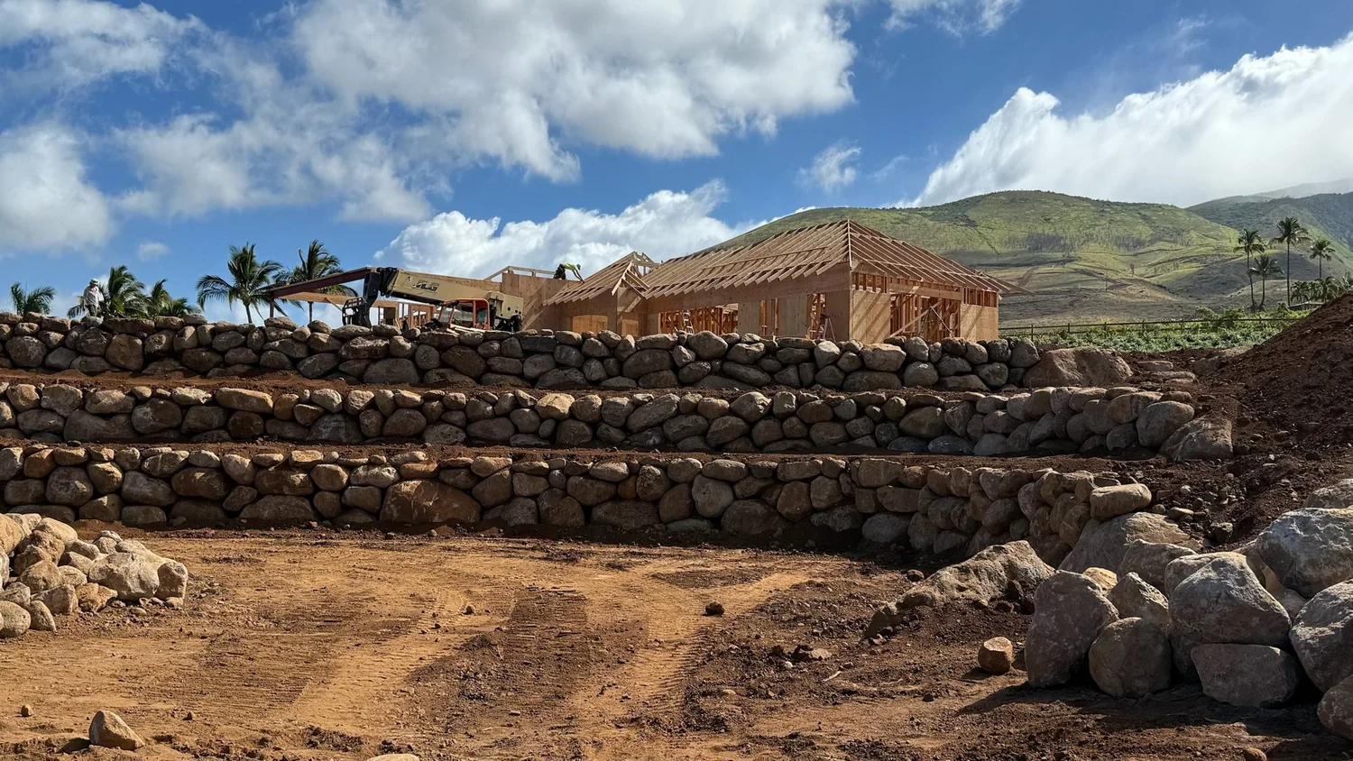 Hand-set stone terrace walls and grading during a Blooming Gardens installation on Maui