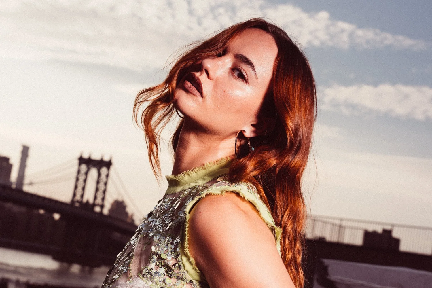 Johnny in a green embellished top, looking back with a bridge and open sky behind her