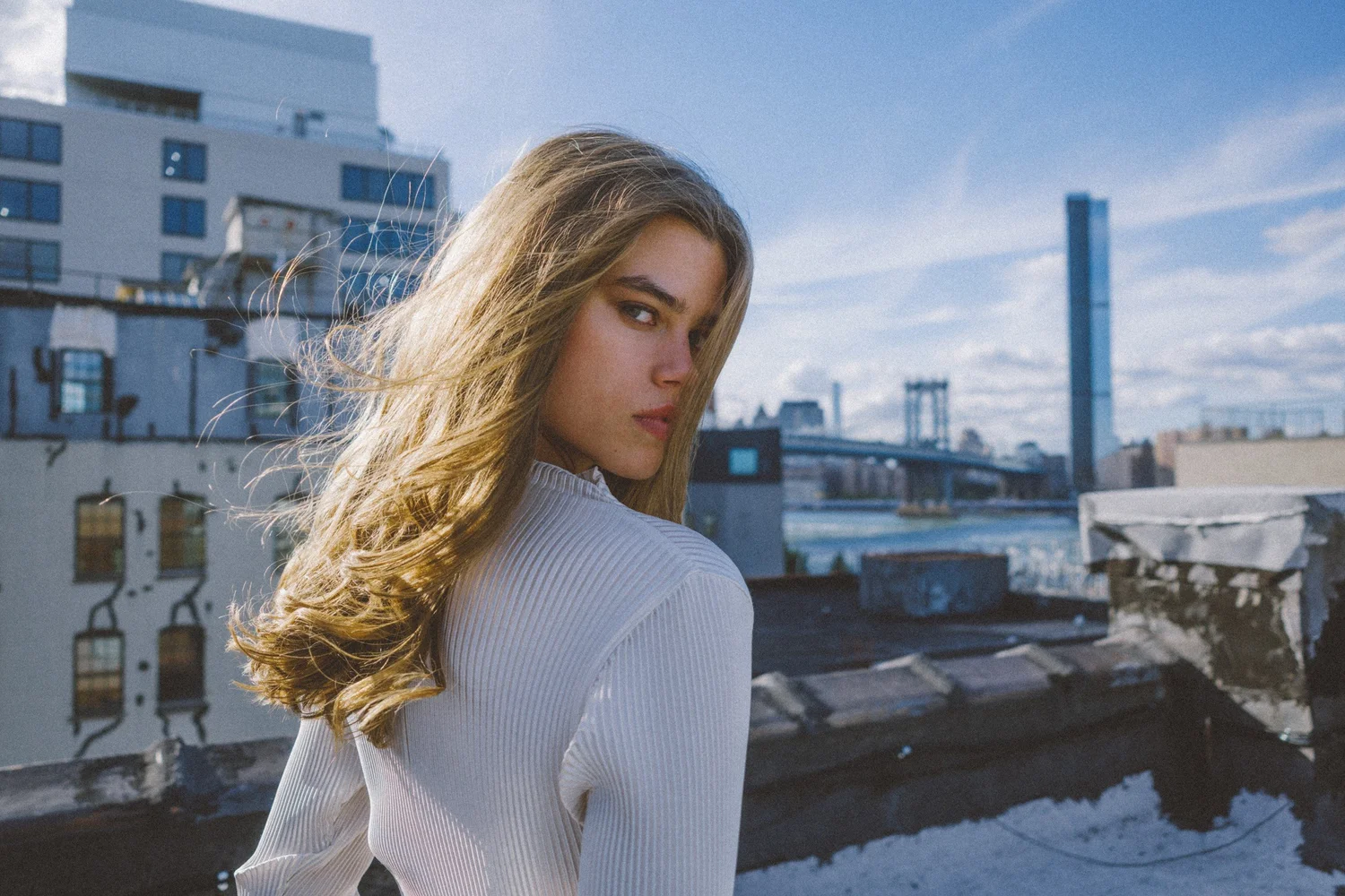 Cydney looking over her shoulder on a rooftop with a bridge and skyline behind her