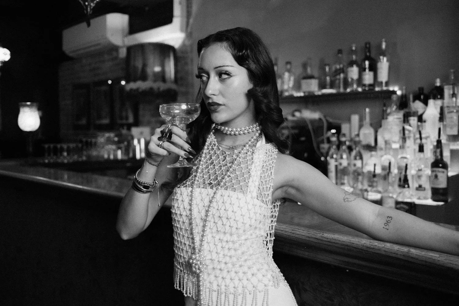 Black-and-white portrait of Eden looking sideways while holding a glass at the bar