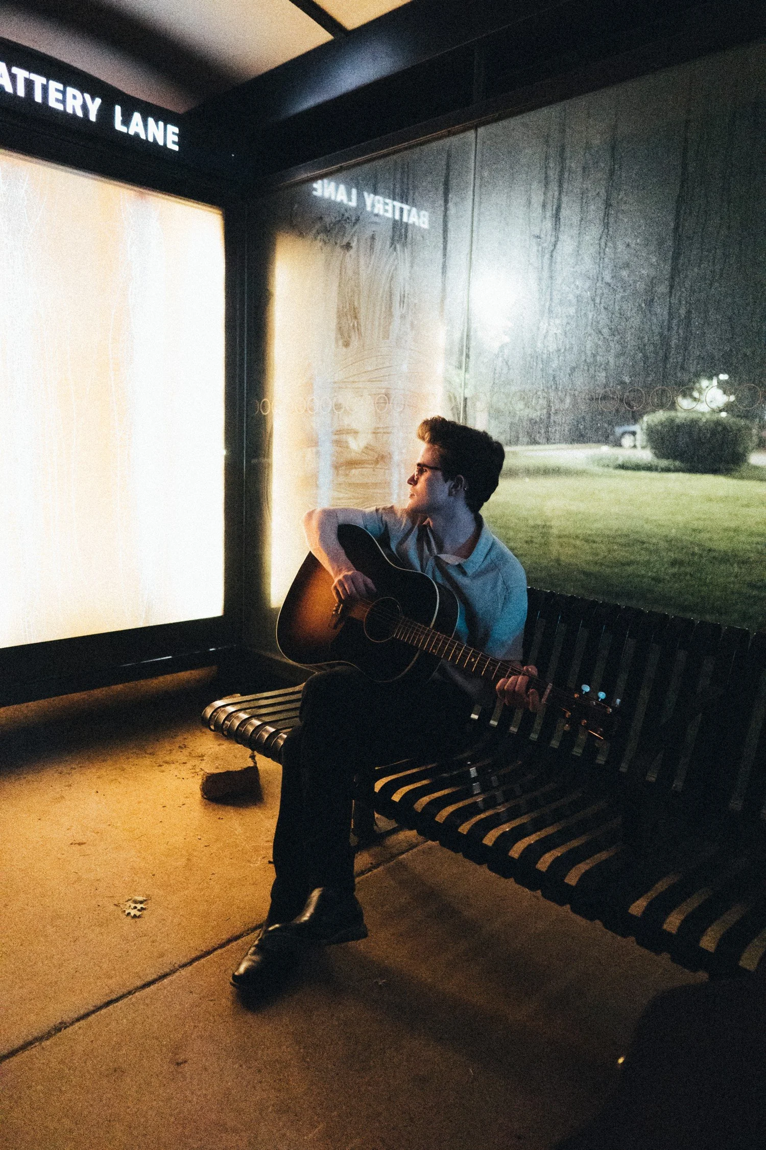 Zack Keim seated with an acoustic guitar in an illuminated shelter at night.
