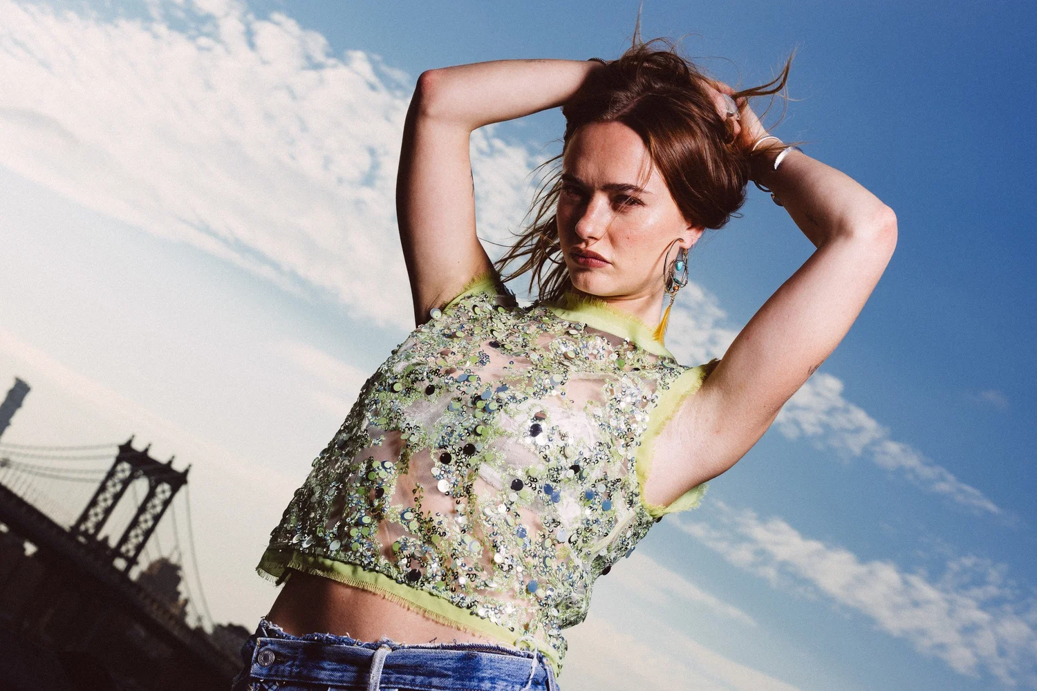 Johnny raising her arms in a green embellished top against blue sky