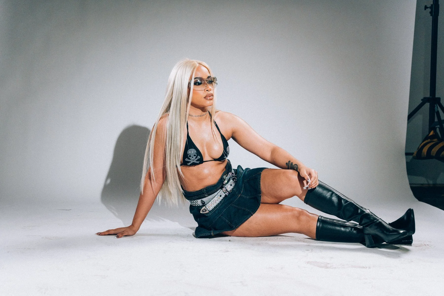 Rose seated on a pale studio floor wearing black boots and sunglasses