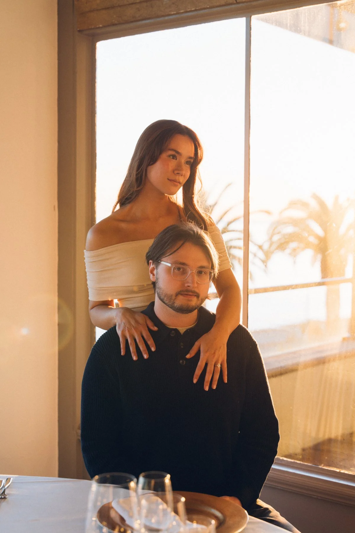 Hannah standing behind Garrett beside a bright window