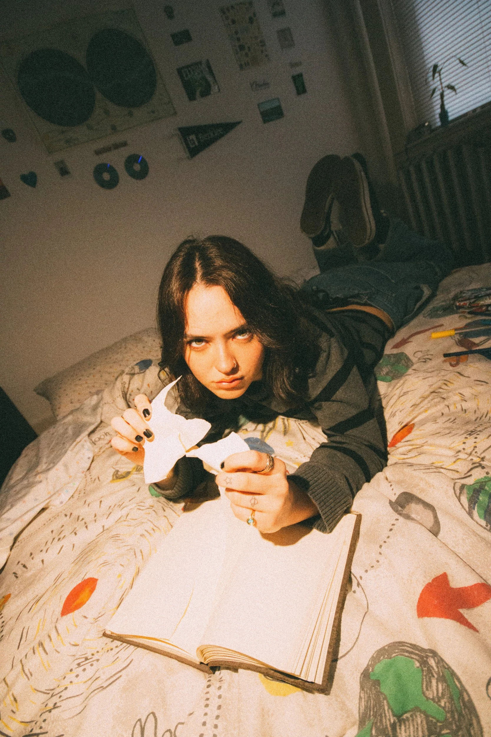 Jenna Doe tearing a sheet of paper above an open notebook on a patterned bed.