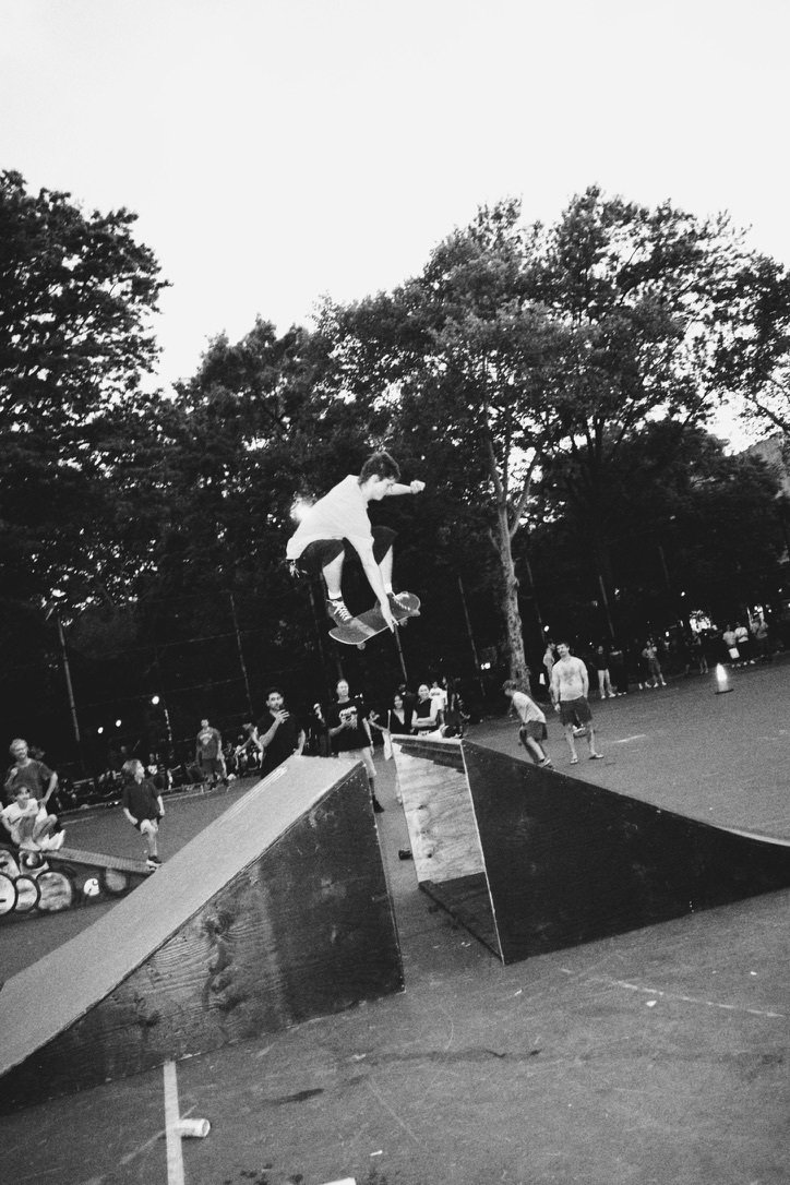 Black-and-white wide view of a skater jumping above a paved area