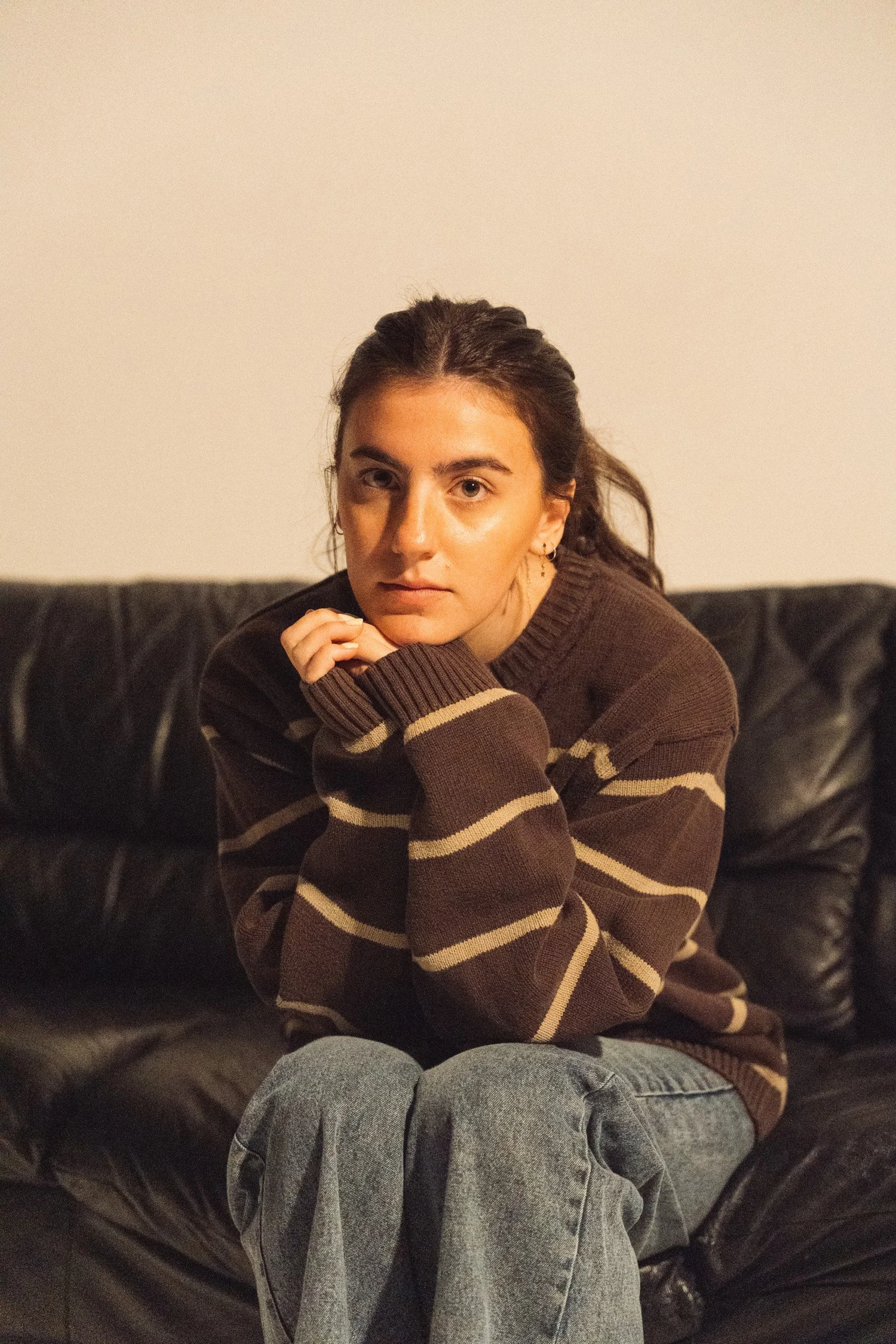 Avery Lynch in a striped sweater, resting her chin on her hand on a black couch.
