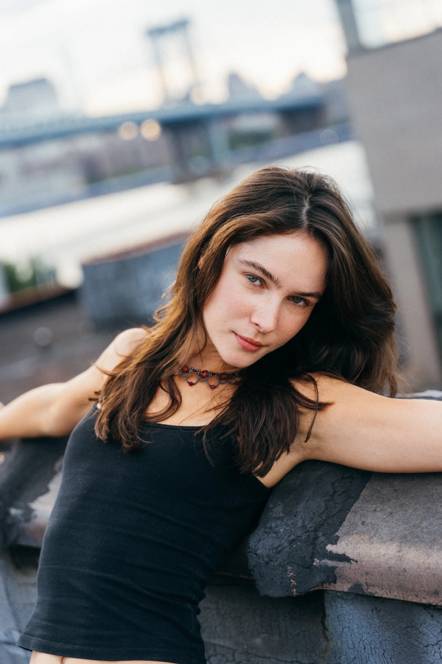 Close portrait of Amanda leaning across a rooftop wall with the bridge softly blurred behind her
