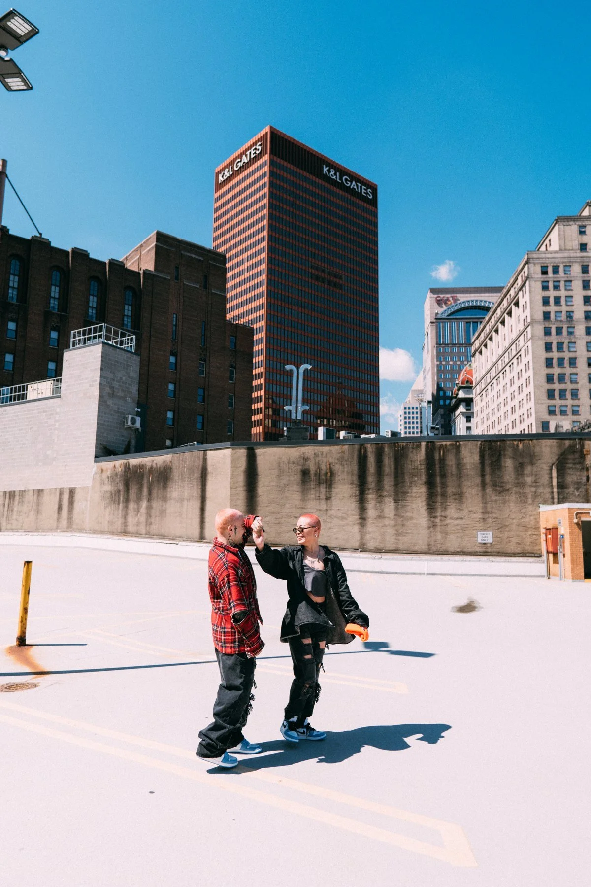 Ash and AJ standing playfully together in an open paved city space
