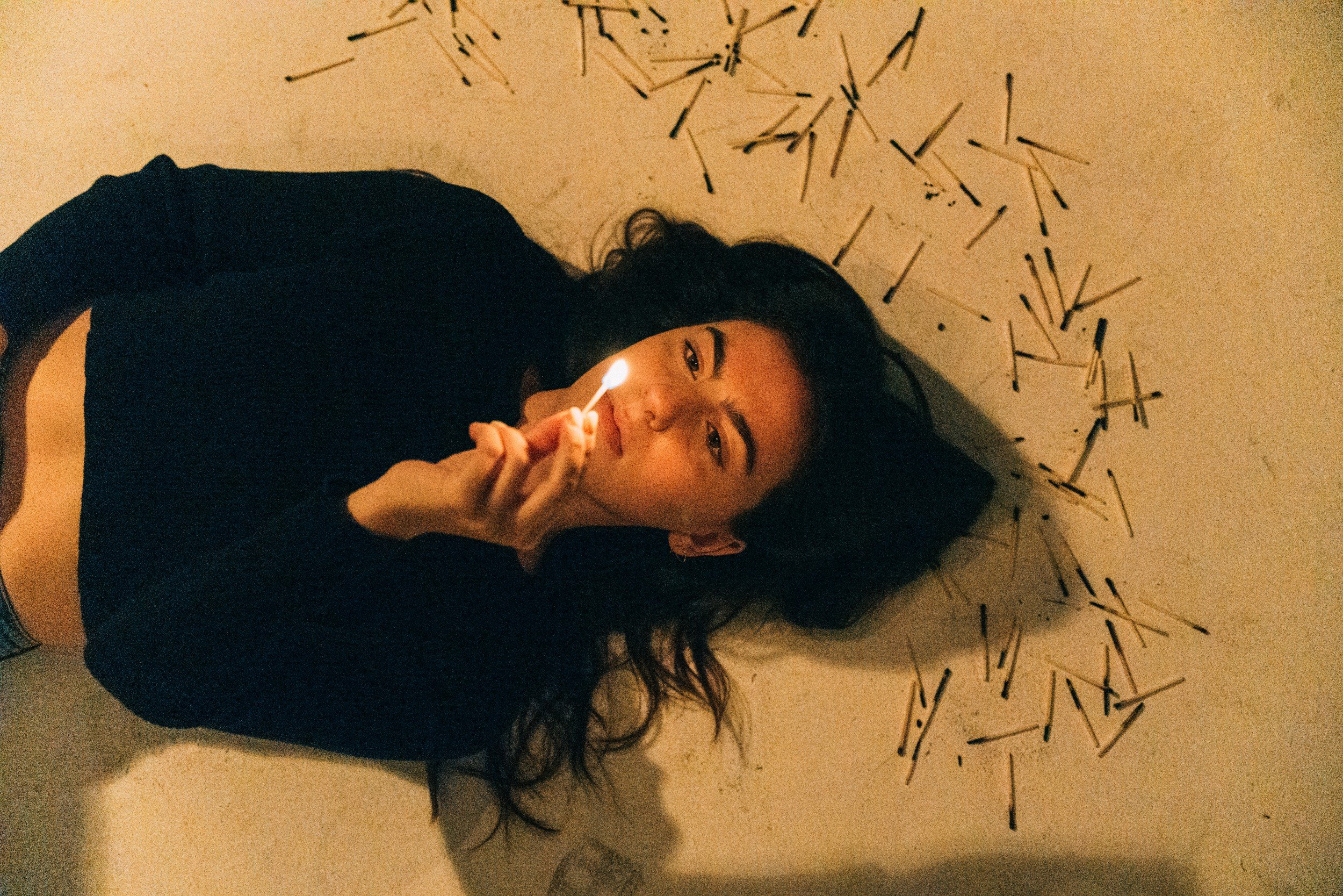 Avery Lynch lying among scattered matches, holding a flame near her face.