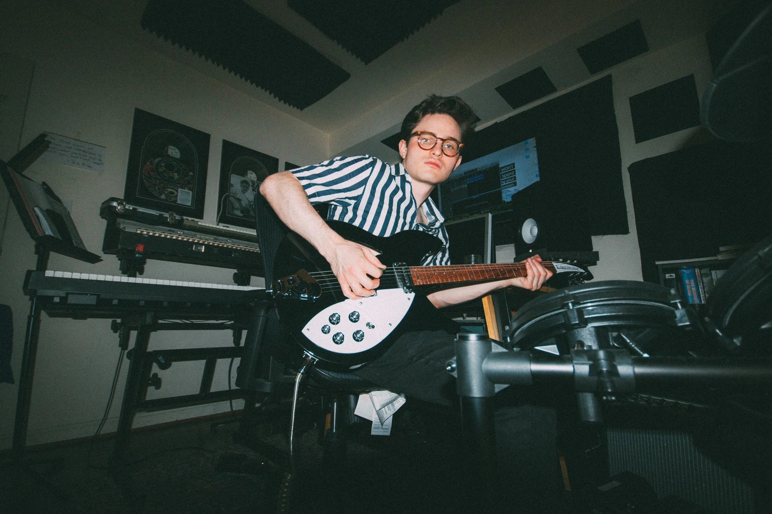 Zack Keim holding an electric guitar in a room with keyboards and acoustic panels.