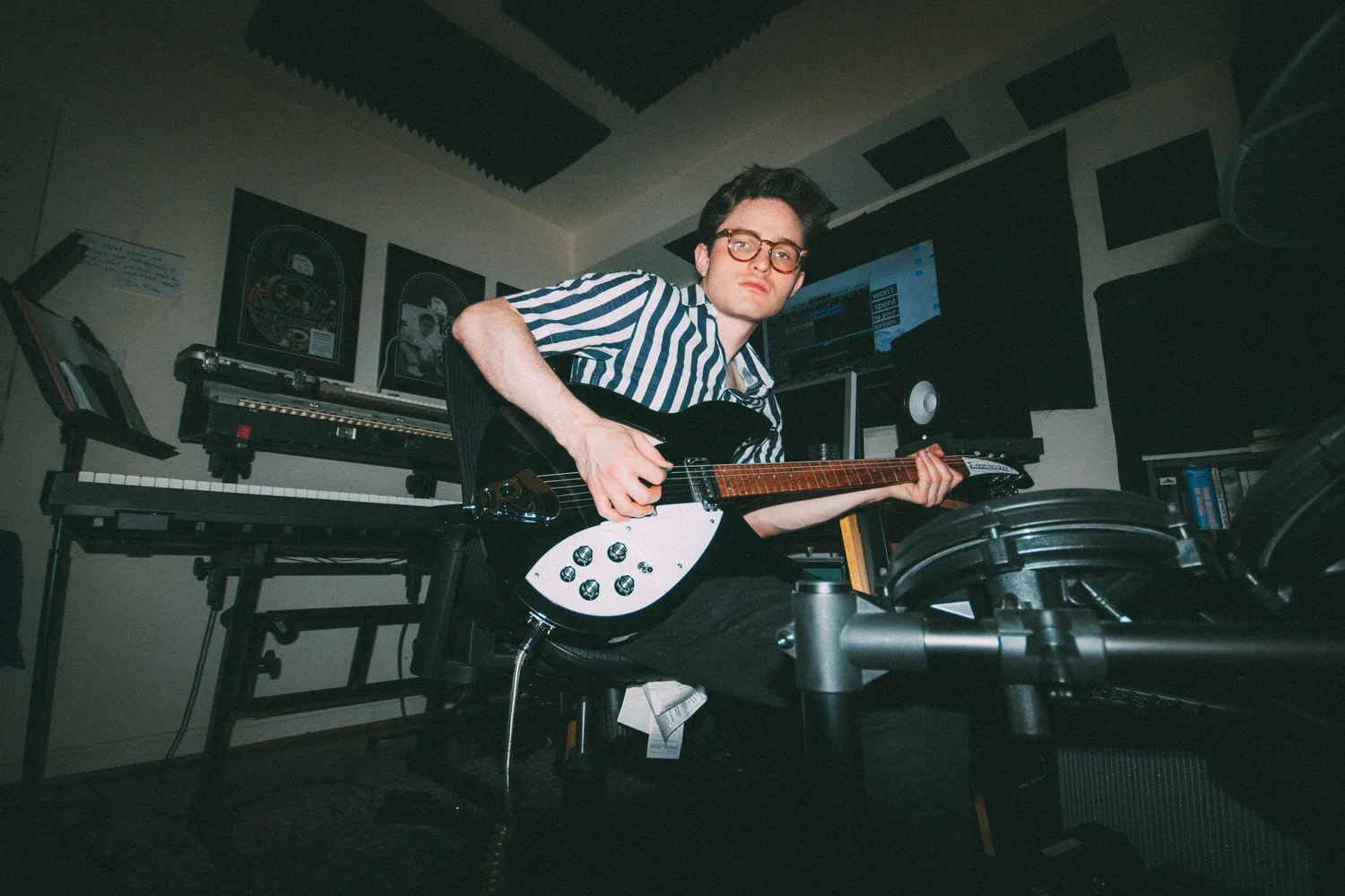 Zack Keim holding an electric guitar in a room with keyboards and acoustic panels.