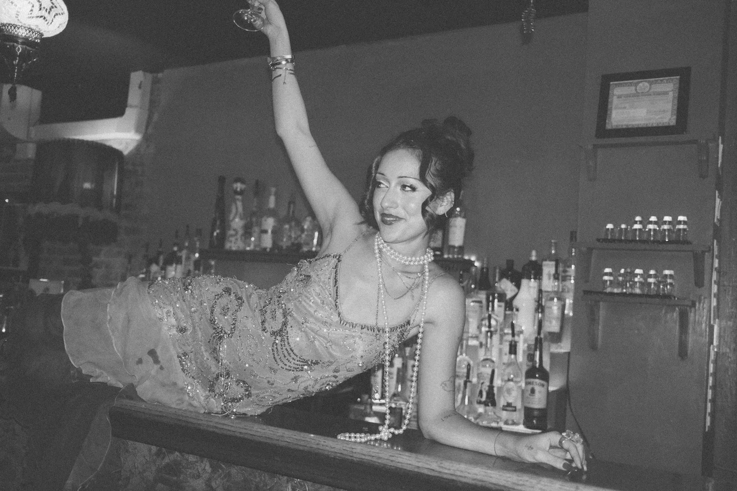 Black-and-white portrait of Eden reclining across the bar with one arm raised