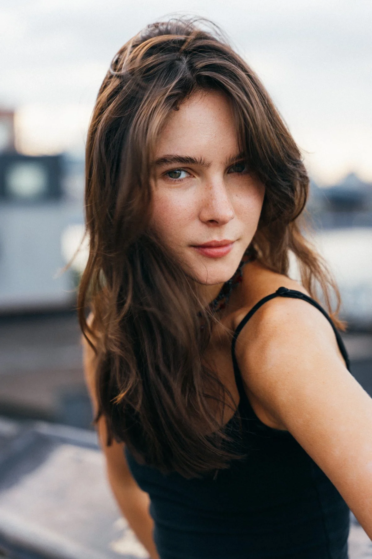 Close rooftop portrait of Amanda in a black tank top, with warm buildings softly blurred behind her