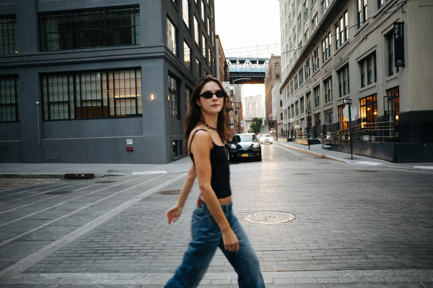 Amanda wearing sunglasses and walking through a city street lined with tall buildings.
