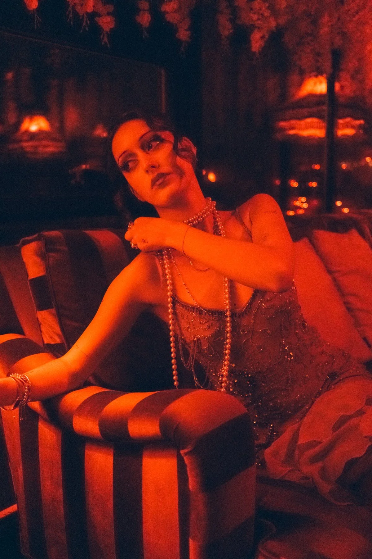 Eden seated in a striped armchair under deep orange-red light