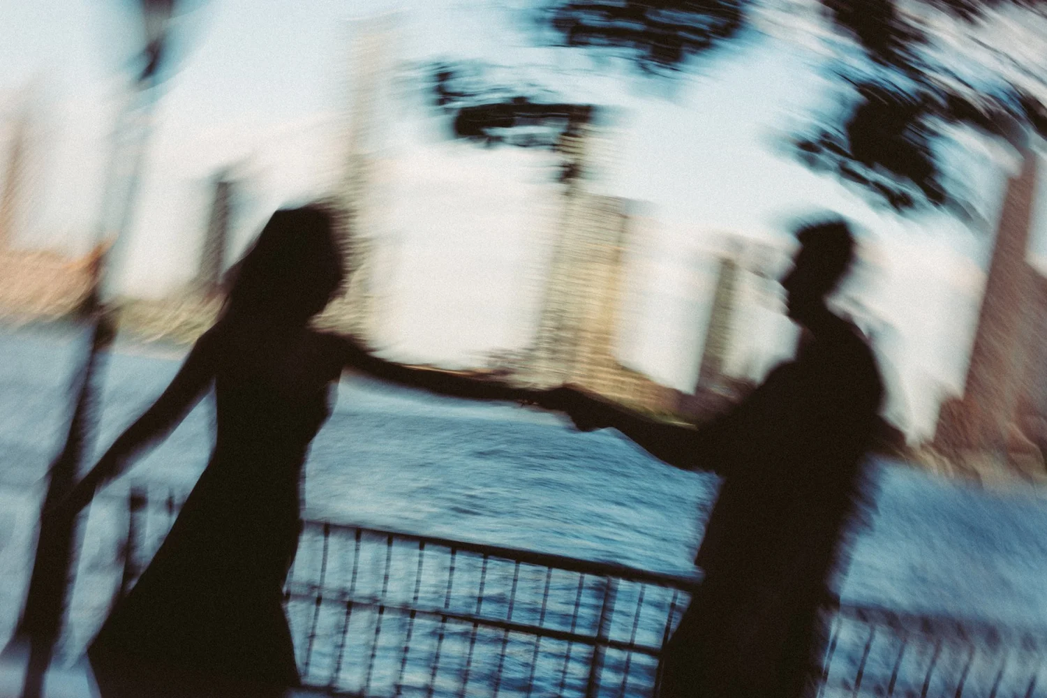 Motion-blurred silhouettes of a couple holding hands, with trees and buildings behind them