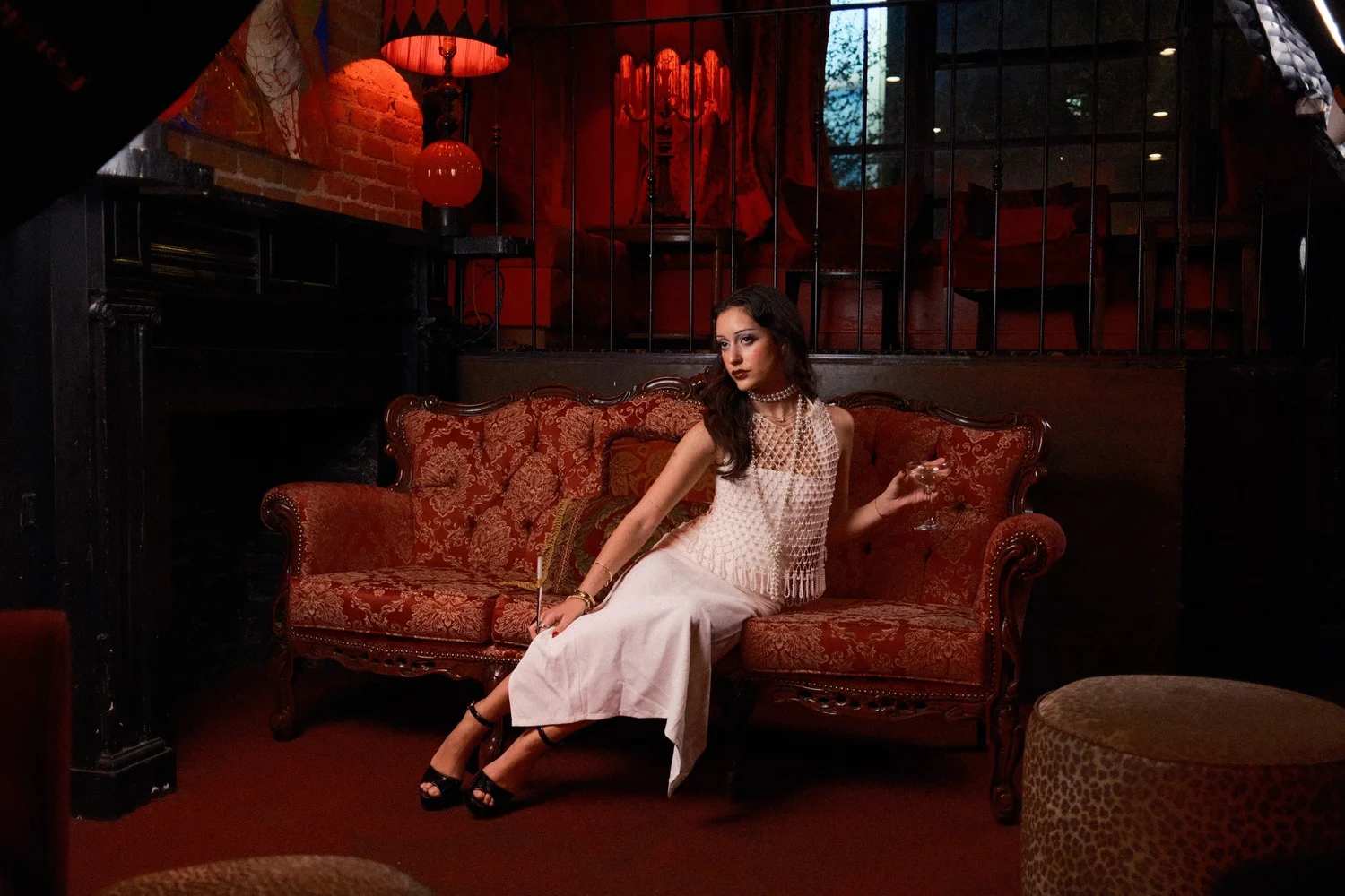 Eden seated on a red sofa in a dark interior with hanging lanterns