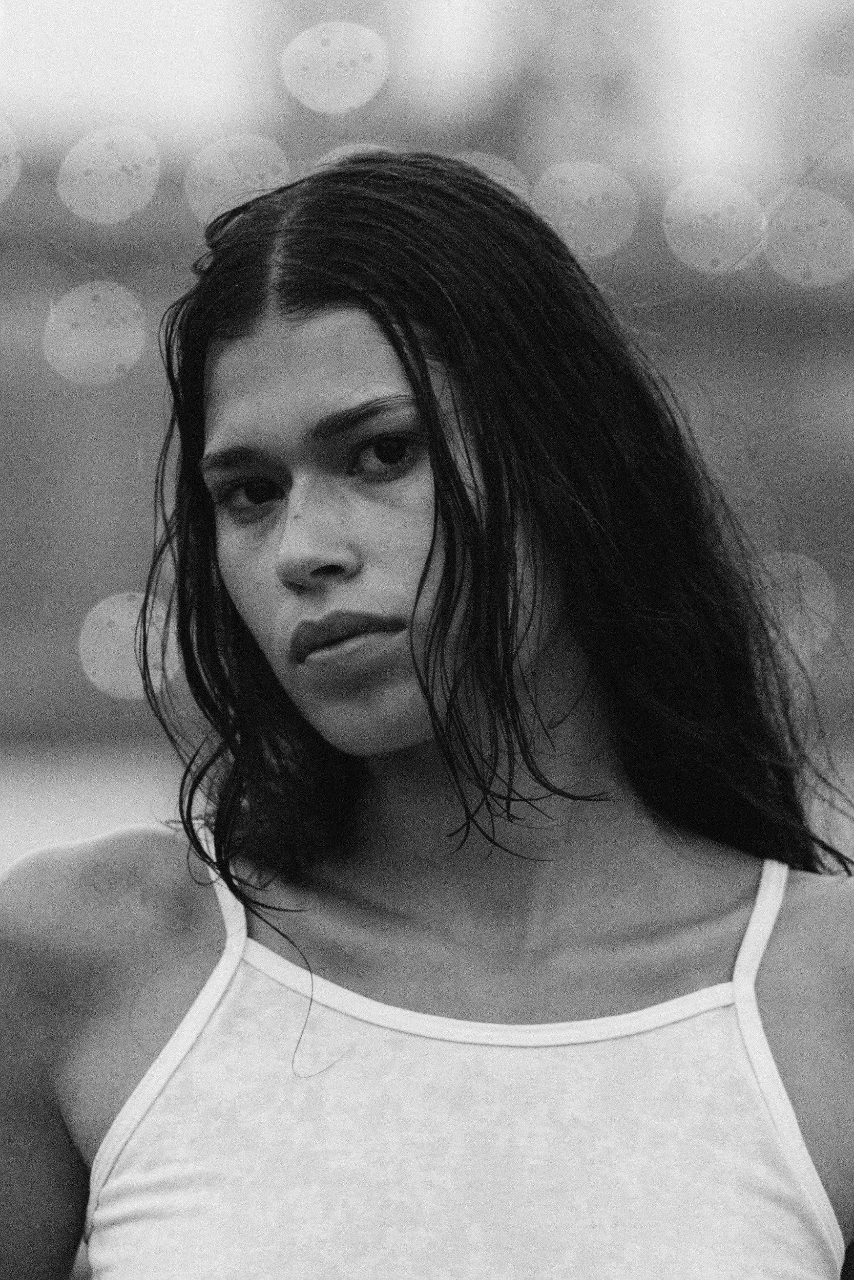 Black-and-white close portrait of Tara with loose hair and bright circles in the background.