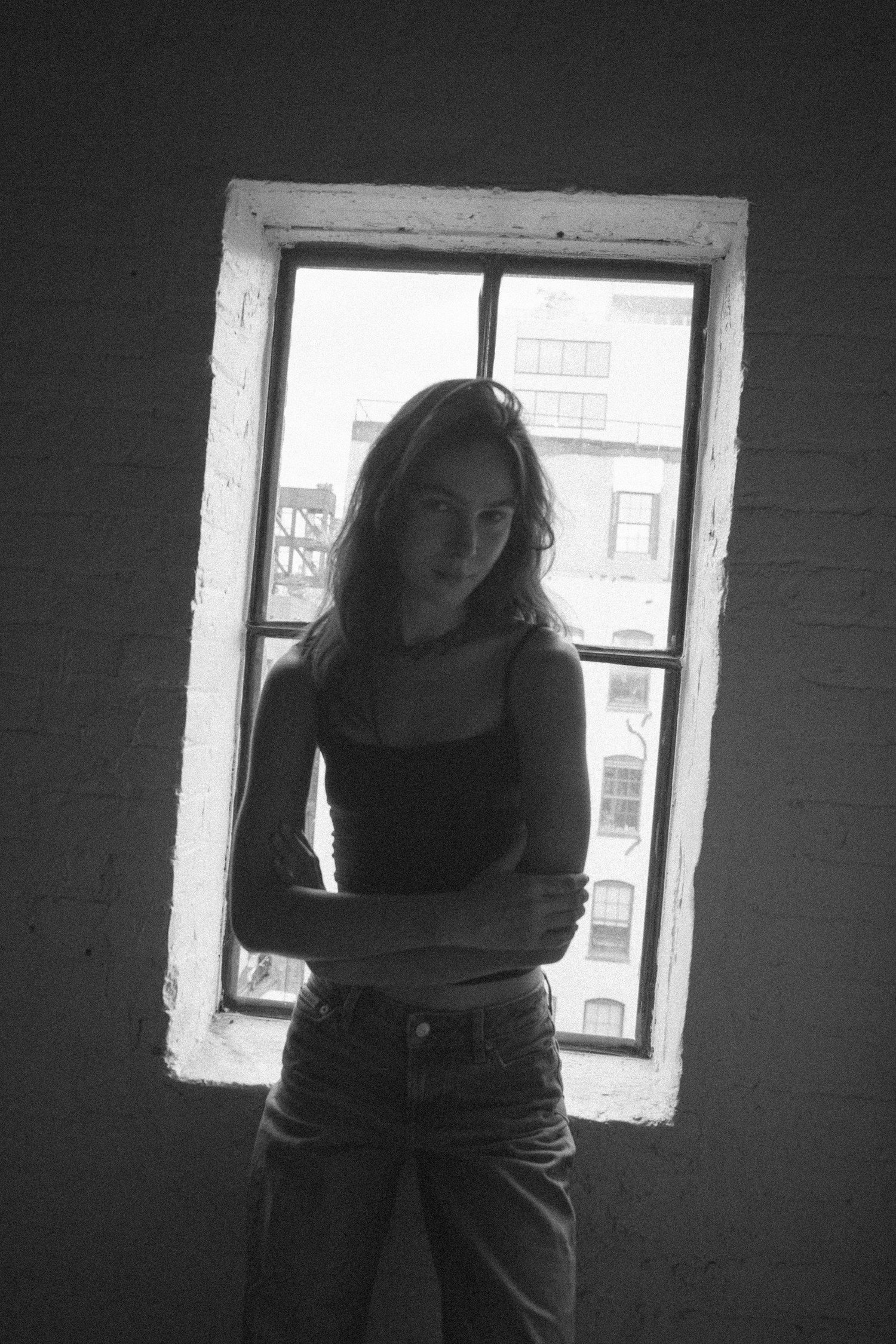 Black and white portrait of Amanda with folded arms against a bright window