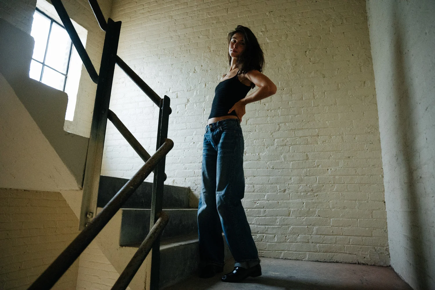 Amanda standing by a stair railing in a white brick interior