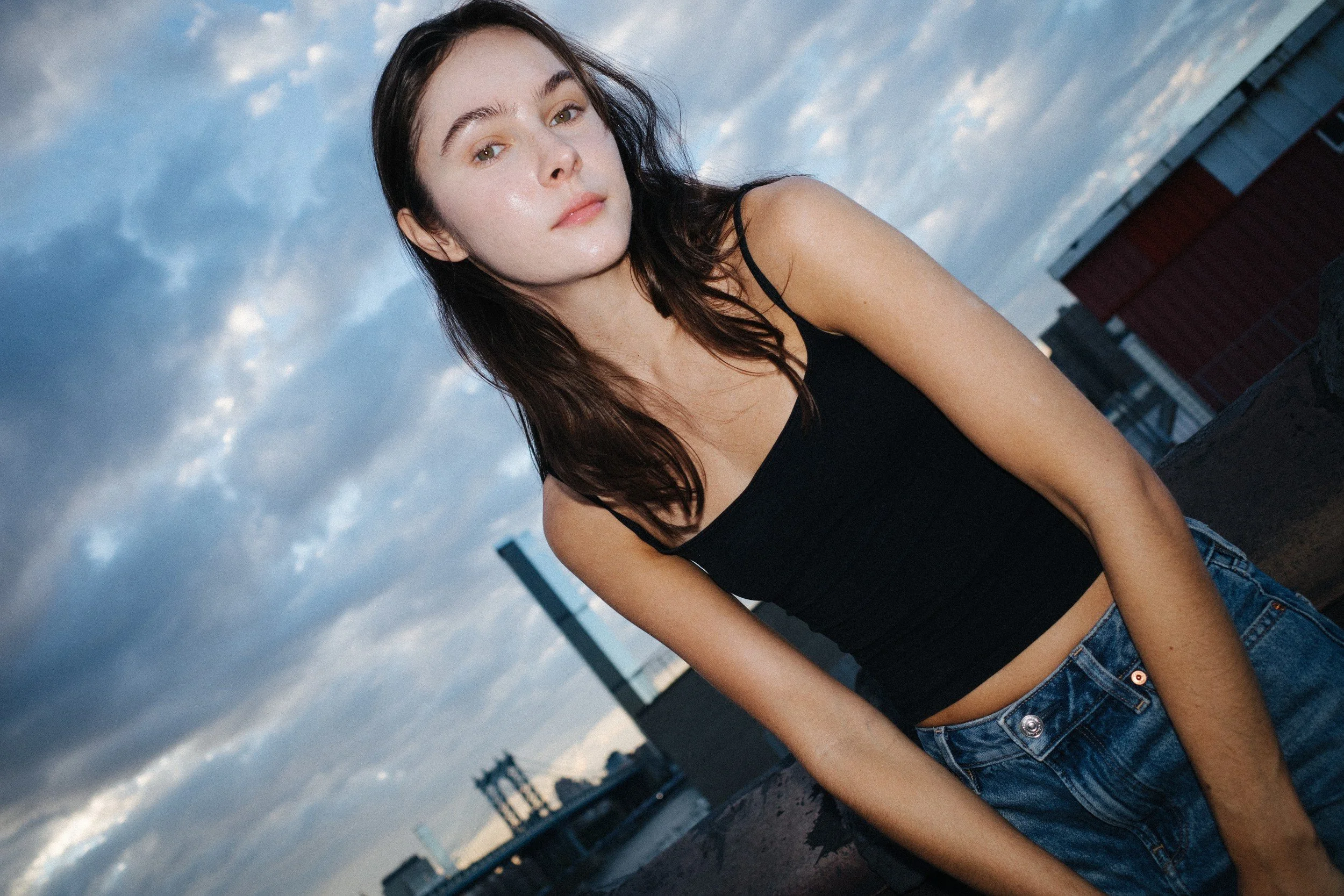 Amanda in a black tank top photographed from a low angle beneath a blue rooftop sky