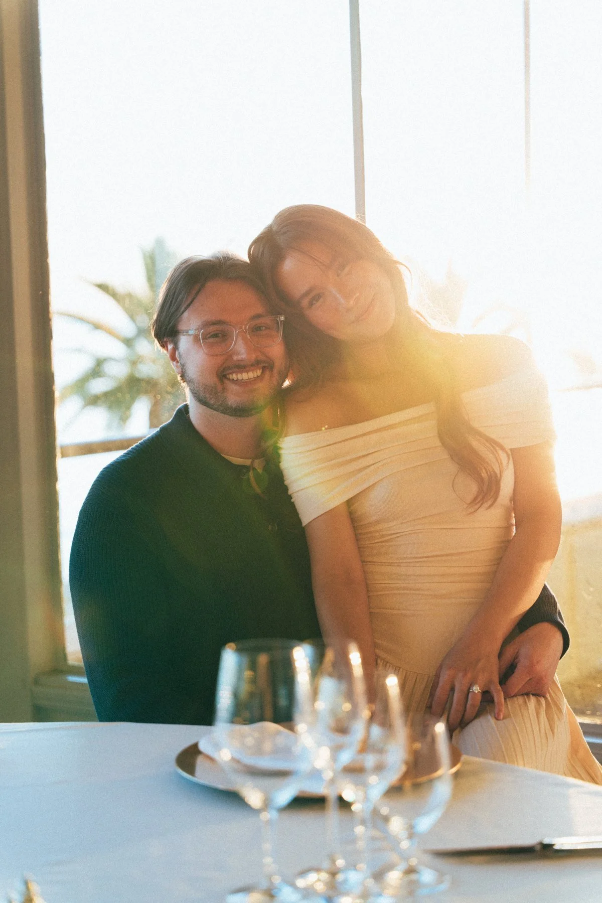Hannah leaning toward Garrett beside a sunlit table