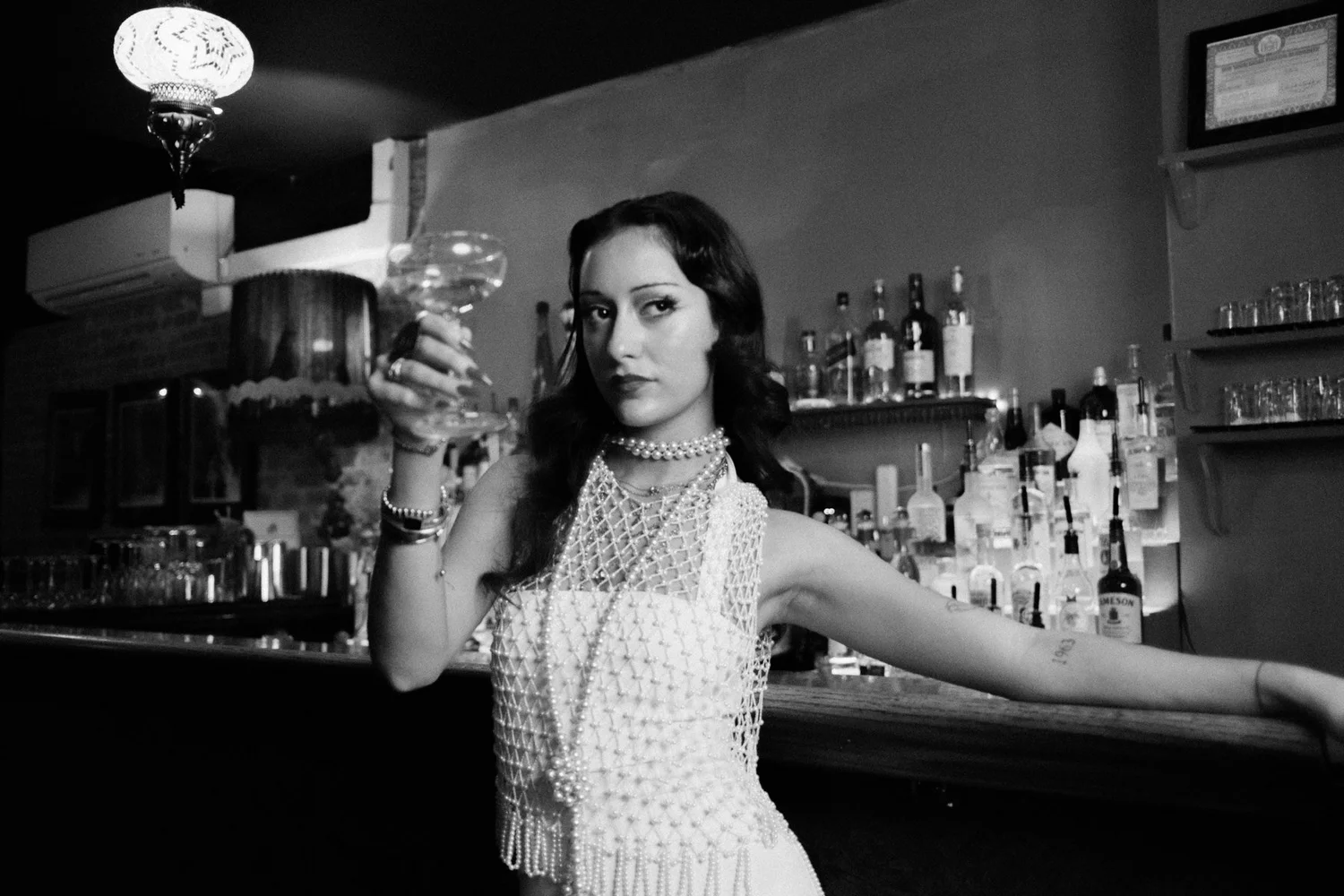 Black-and-white portrait of Eden holding a glass at the bar