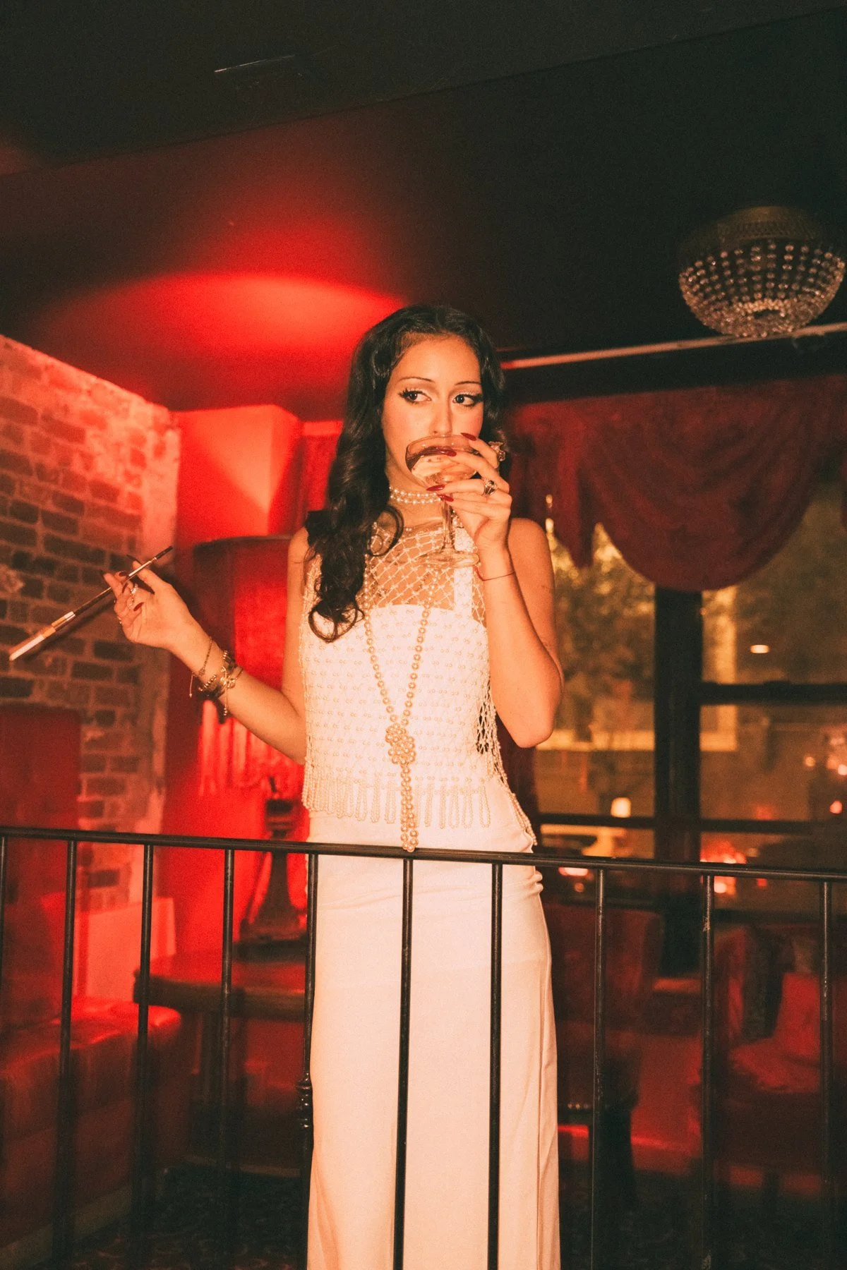 Eden in a white dress beside a railing under red light