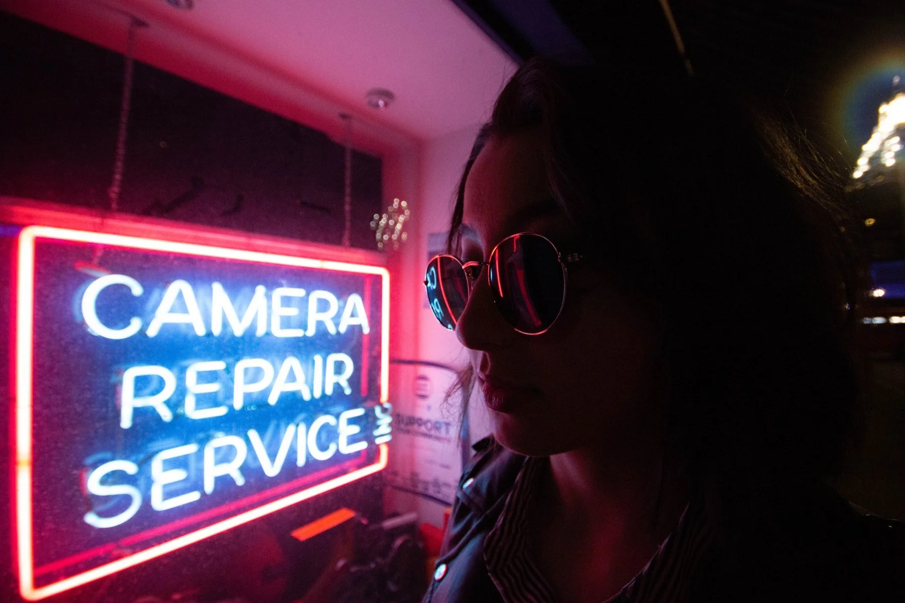 Lauren in sunglasses beside red and blue neon lettering