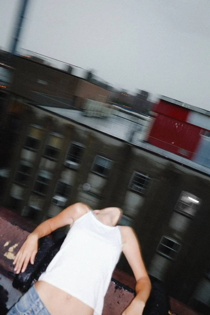 Blurred rooftop portrait of a woman in a white tank top leaning her head back