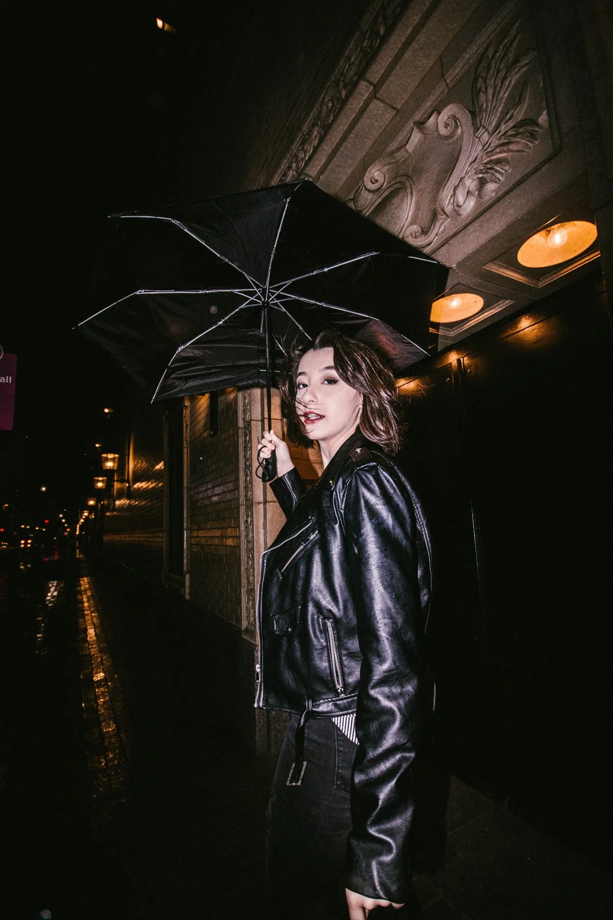 Lauren holding a black umbrella on a wet street at night