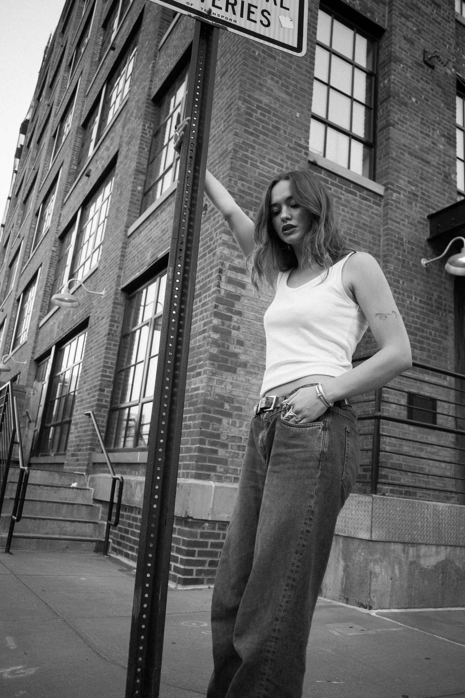 Black and white portrait of Johnny reaching toward a signpost beside a brick building