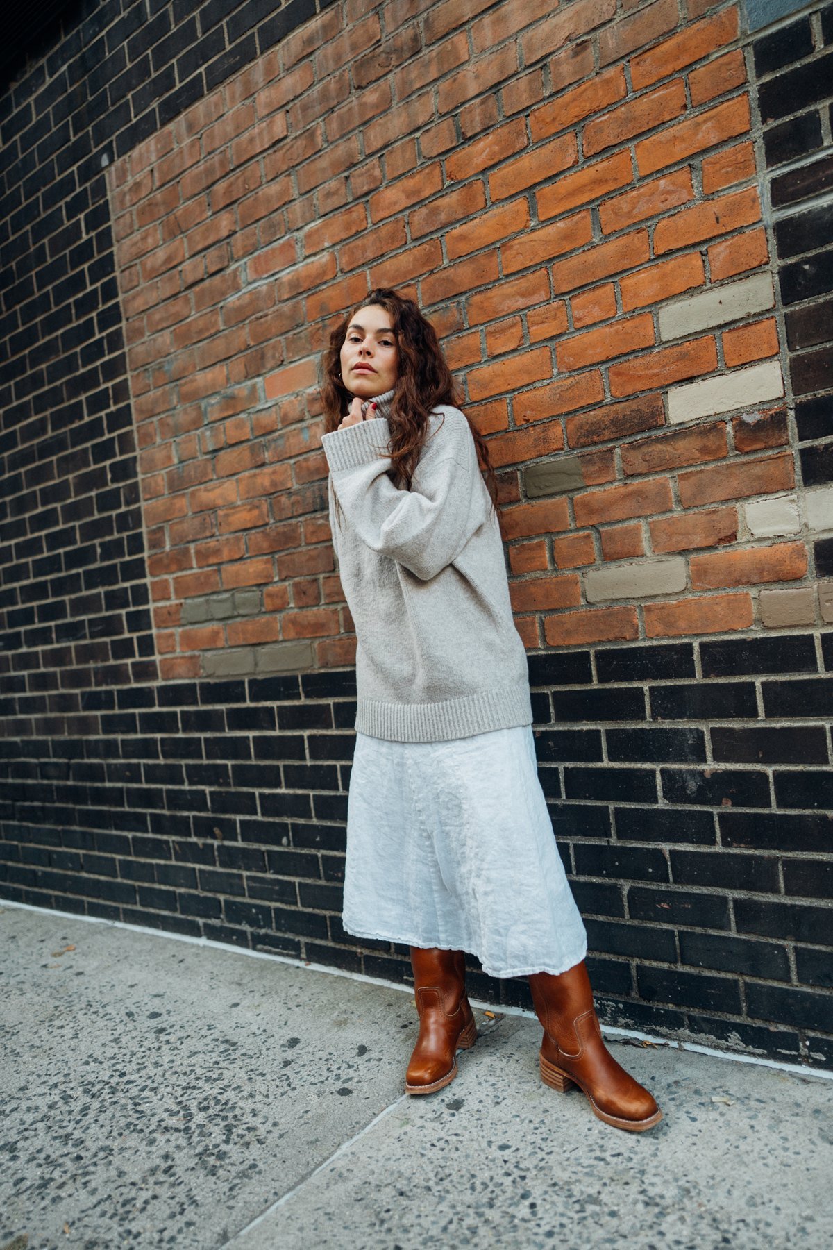 Marley in a sweater and white skirt beside a brick wall