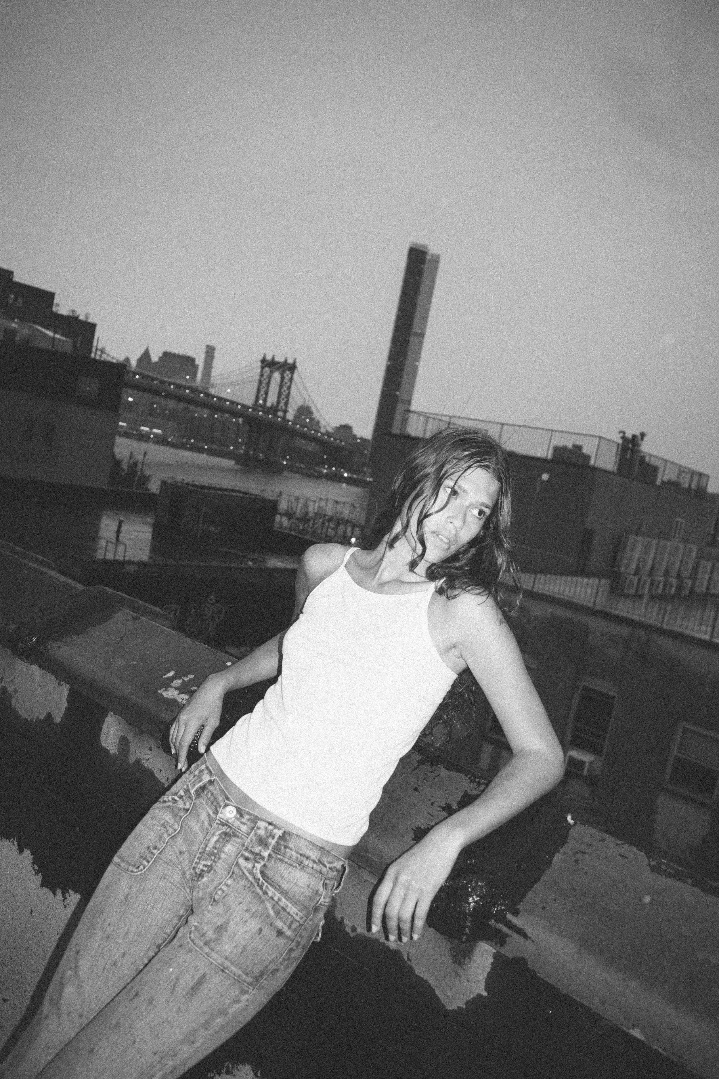 Black and white rooftop portrait of Tara in a white tank top and jeans