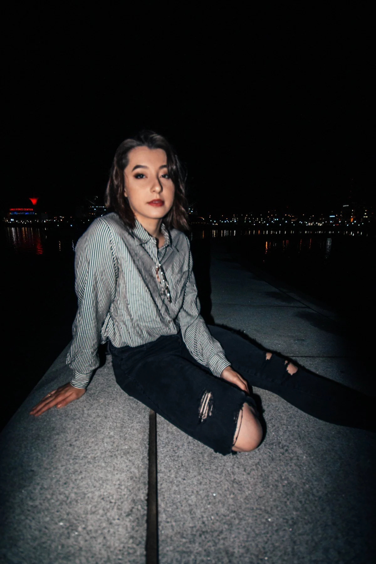 Lauren seated in a striped shirt beside water and distant lights at night