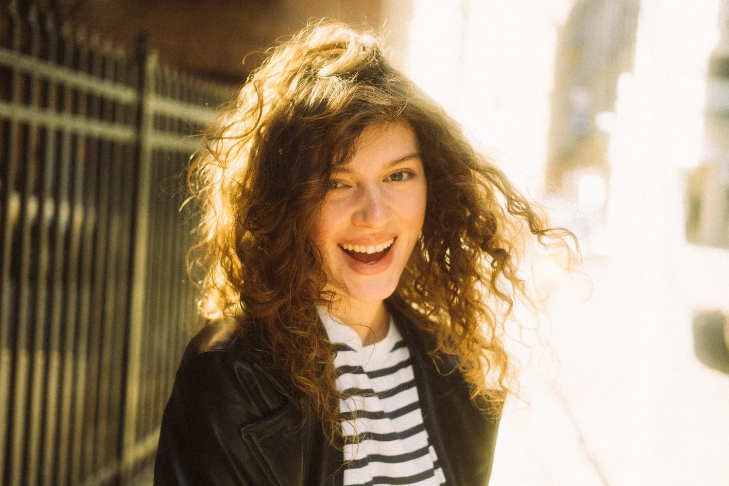 Olenka laughing outdoors with sunlight catching her curly hair