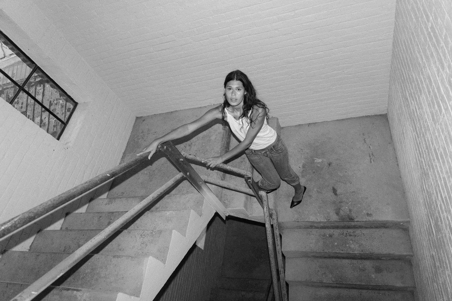 Black-and-white high-angle portrait of Tara holding a stair railing