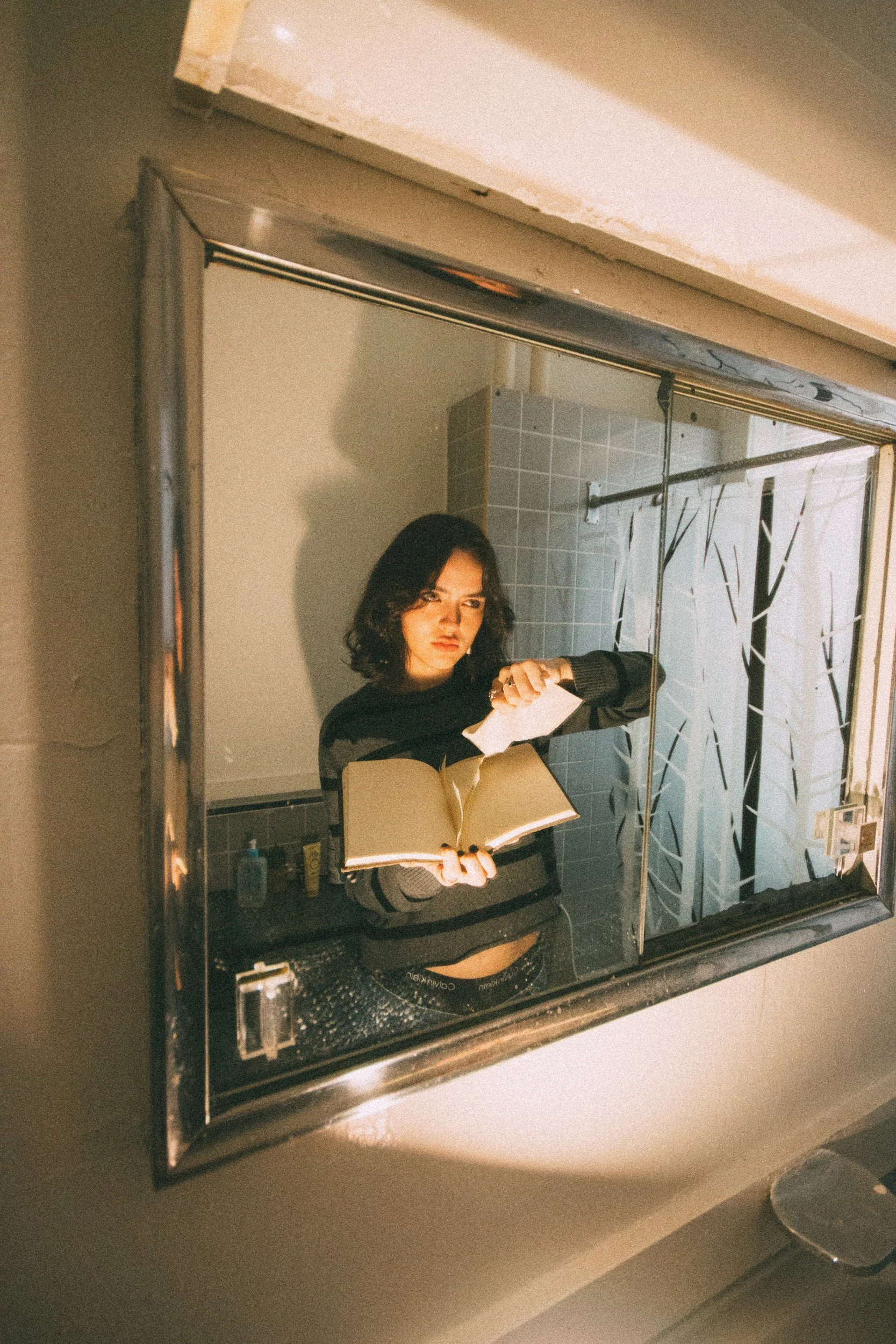 Jenna Doe reflected in a mirror, holding an open notebook and torn paper.
