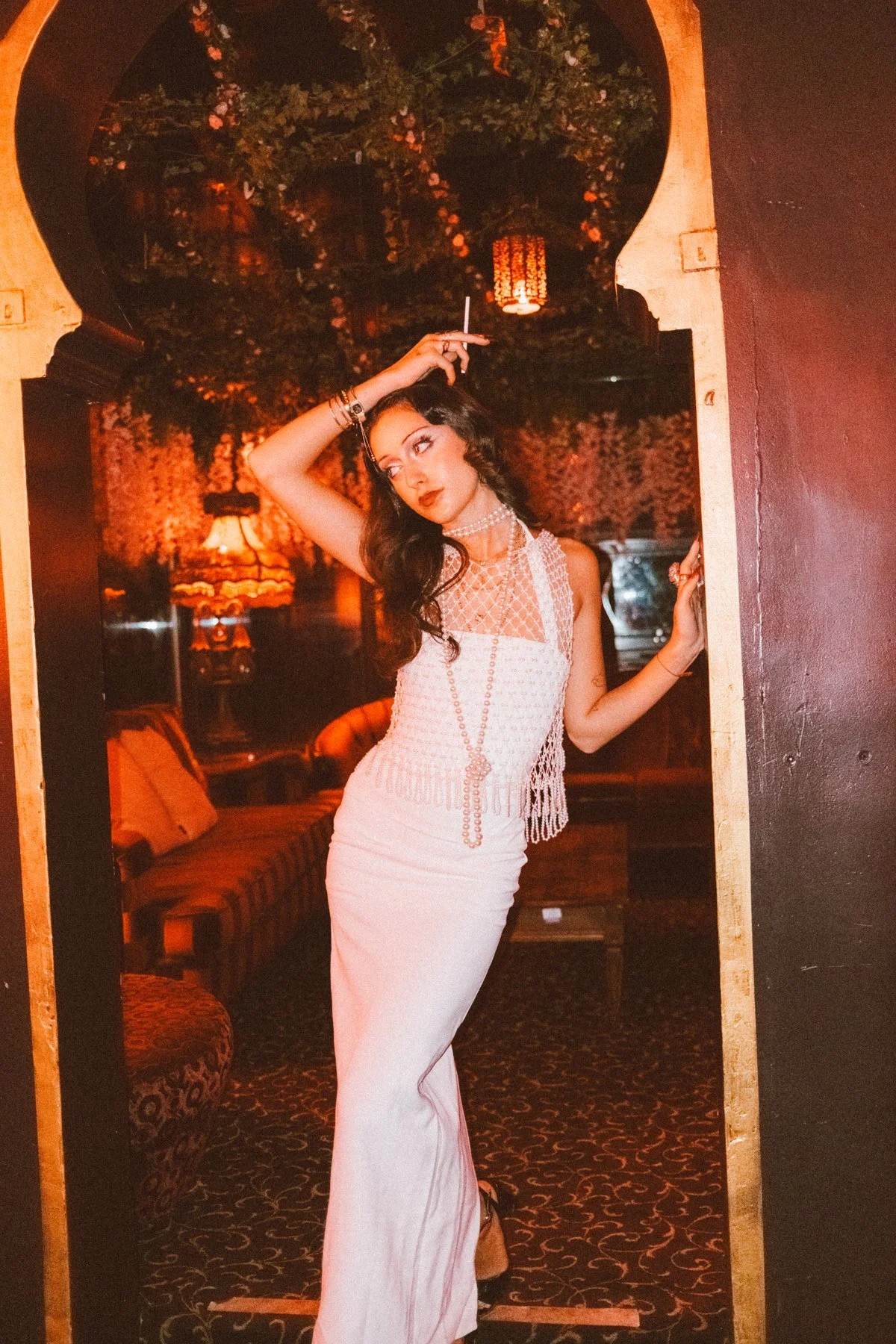 Eden in a white dress raising one arm inside an ornate arch-shaped frame