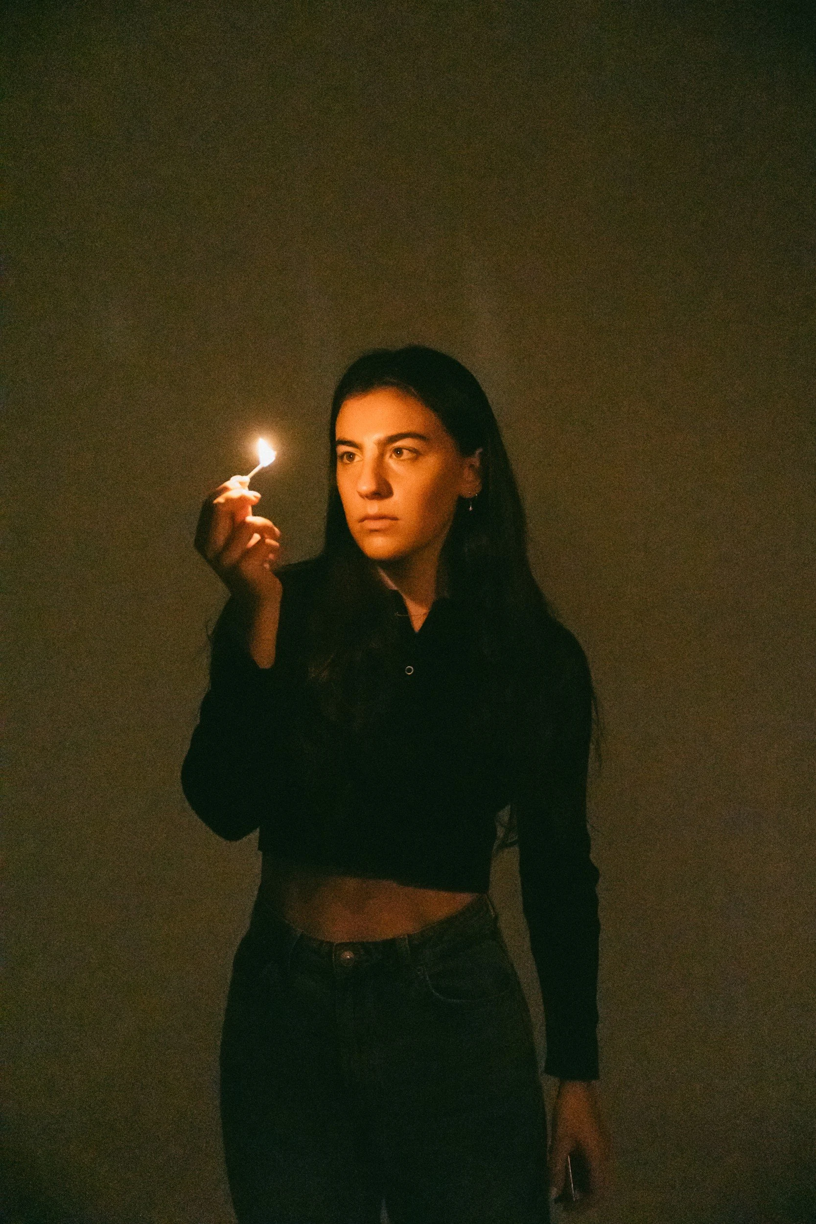 Avery Lynch holding a lit match beside her face against a dark background.