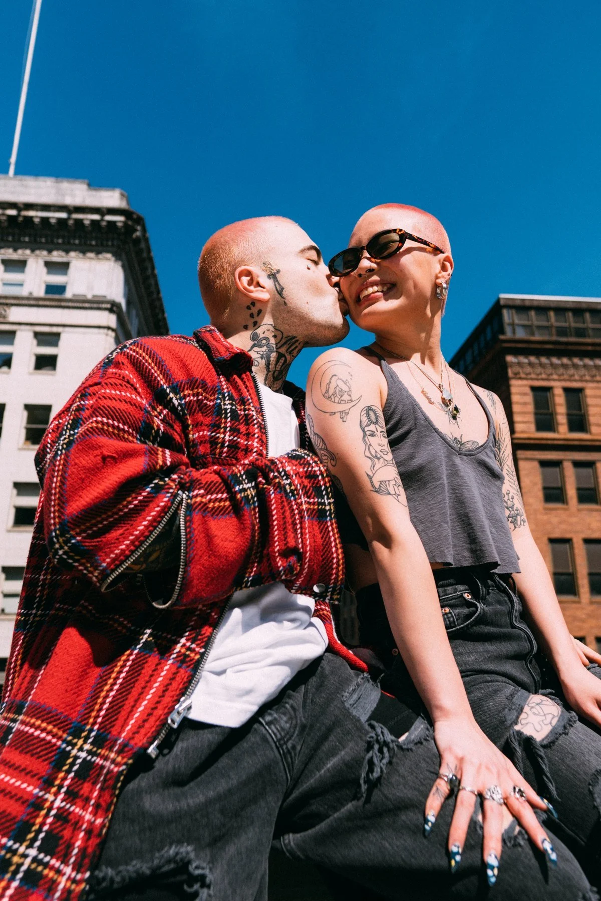 Ash kissing AJ on the cheek beneath a blue sky