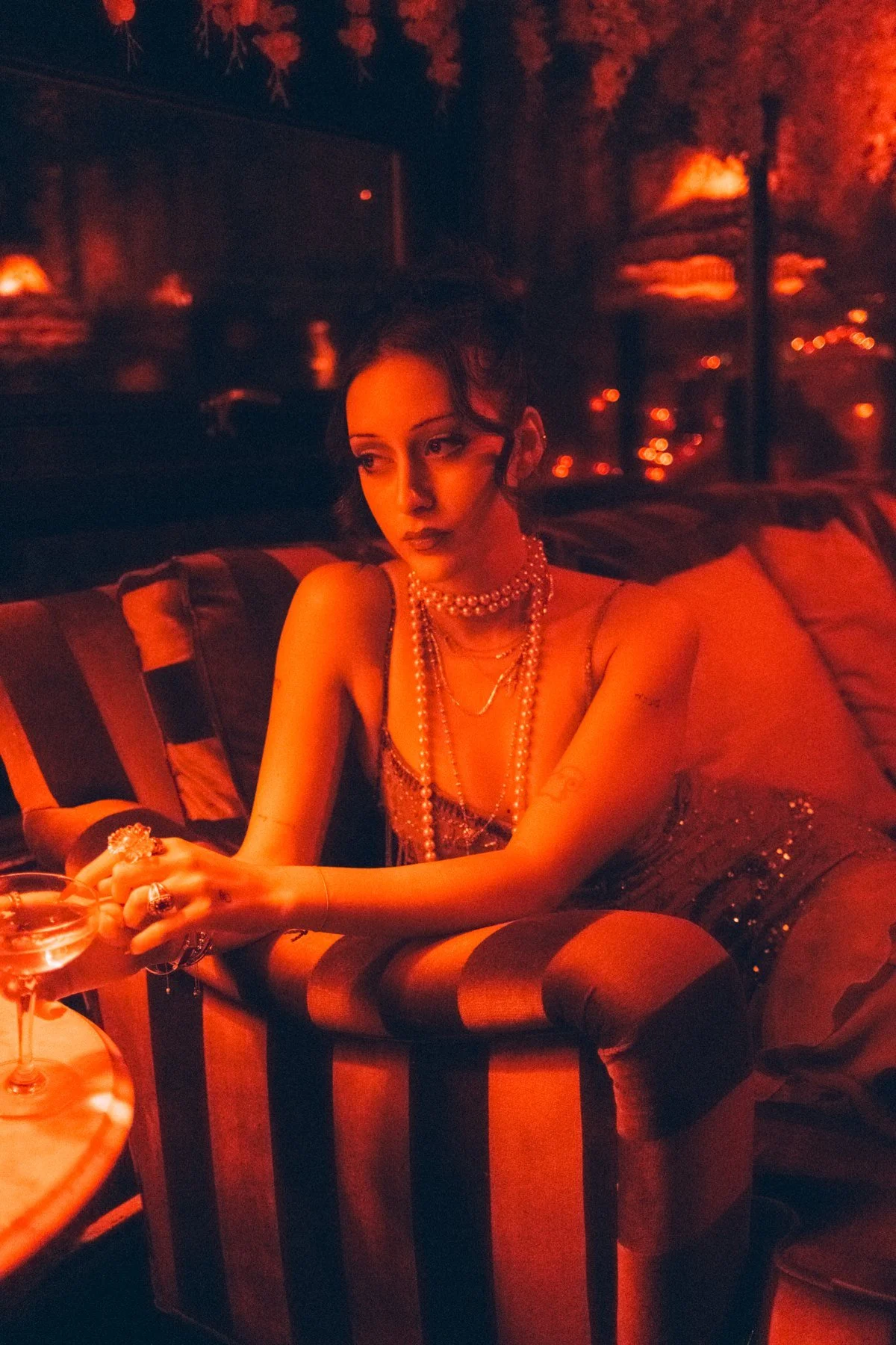 Eden leaning forward over a striped armchair in warm red light