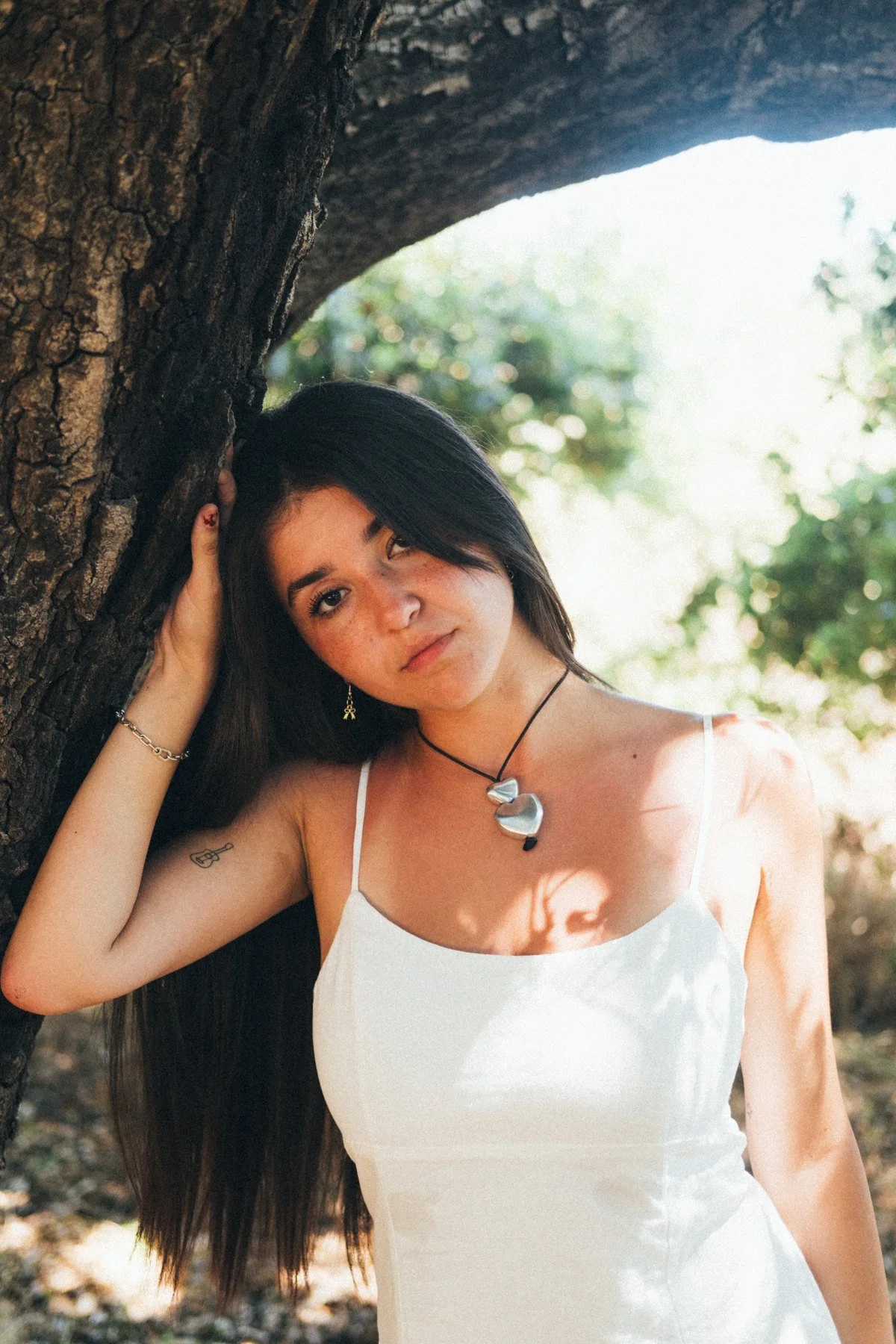 Devon in a white dress beside a tree with soft greenery behind her