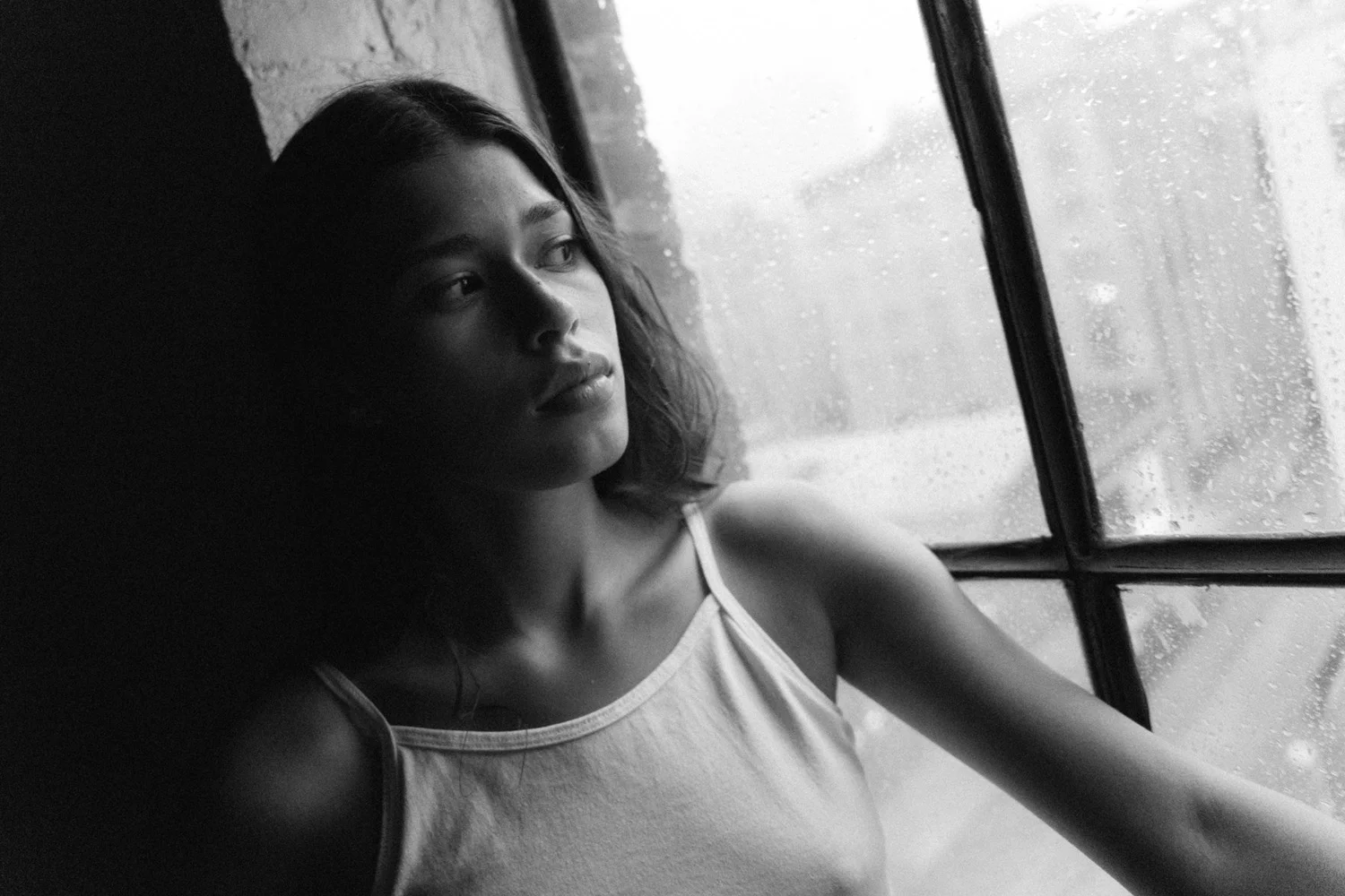 Black-and-white close portrait of Tara looking toward a rain-covered window, with her face partly in shadow