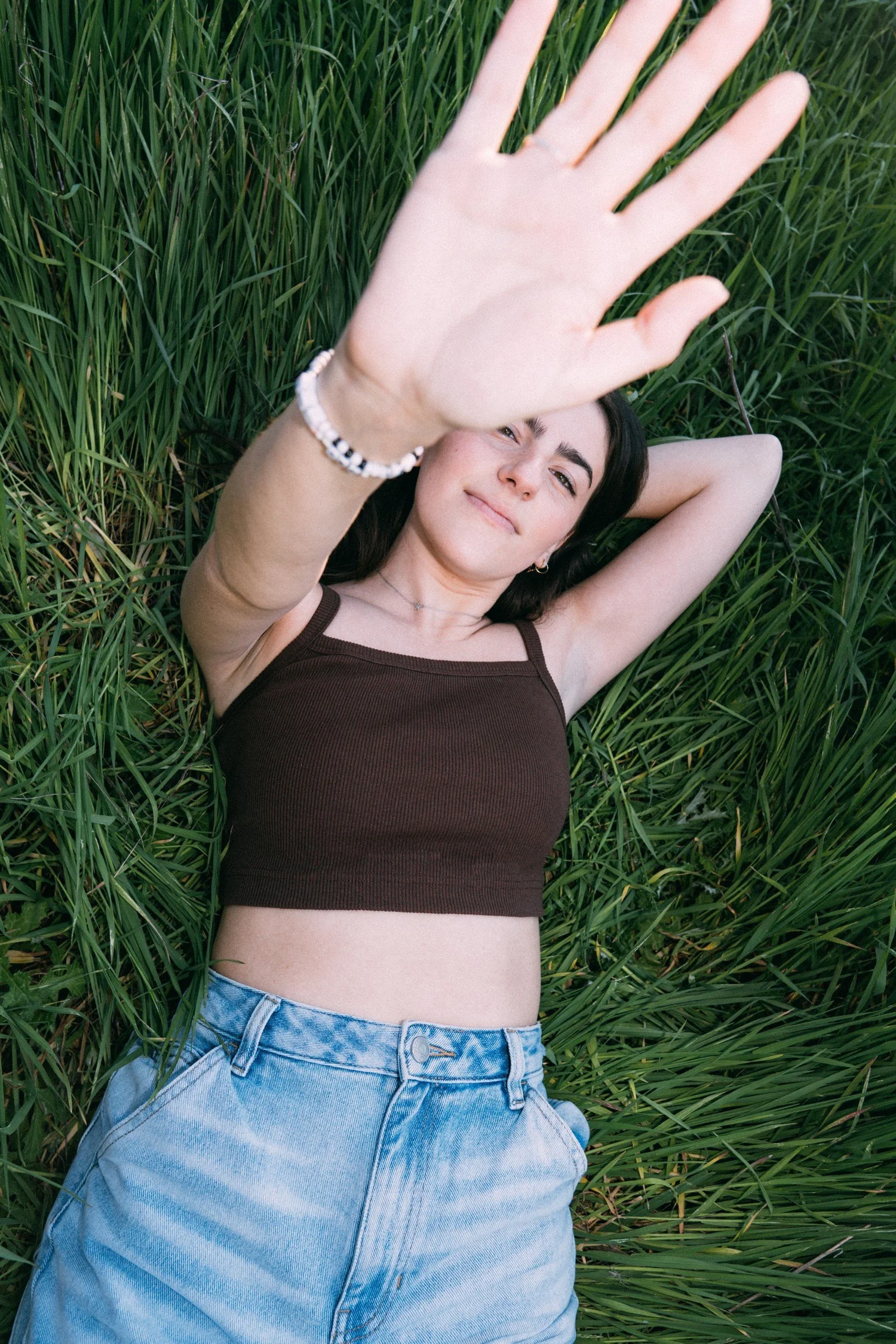 Avery Lynch reclining in grass with one hand reaching toward the camera.