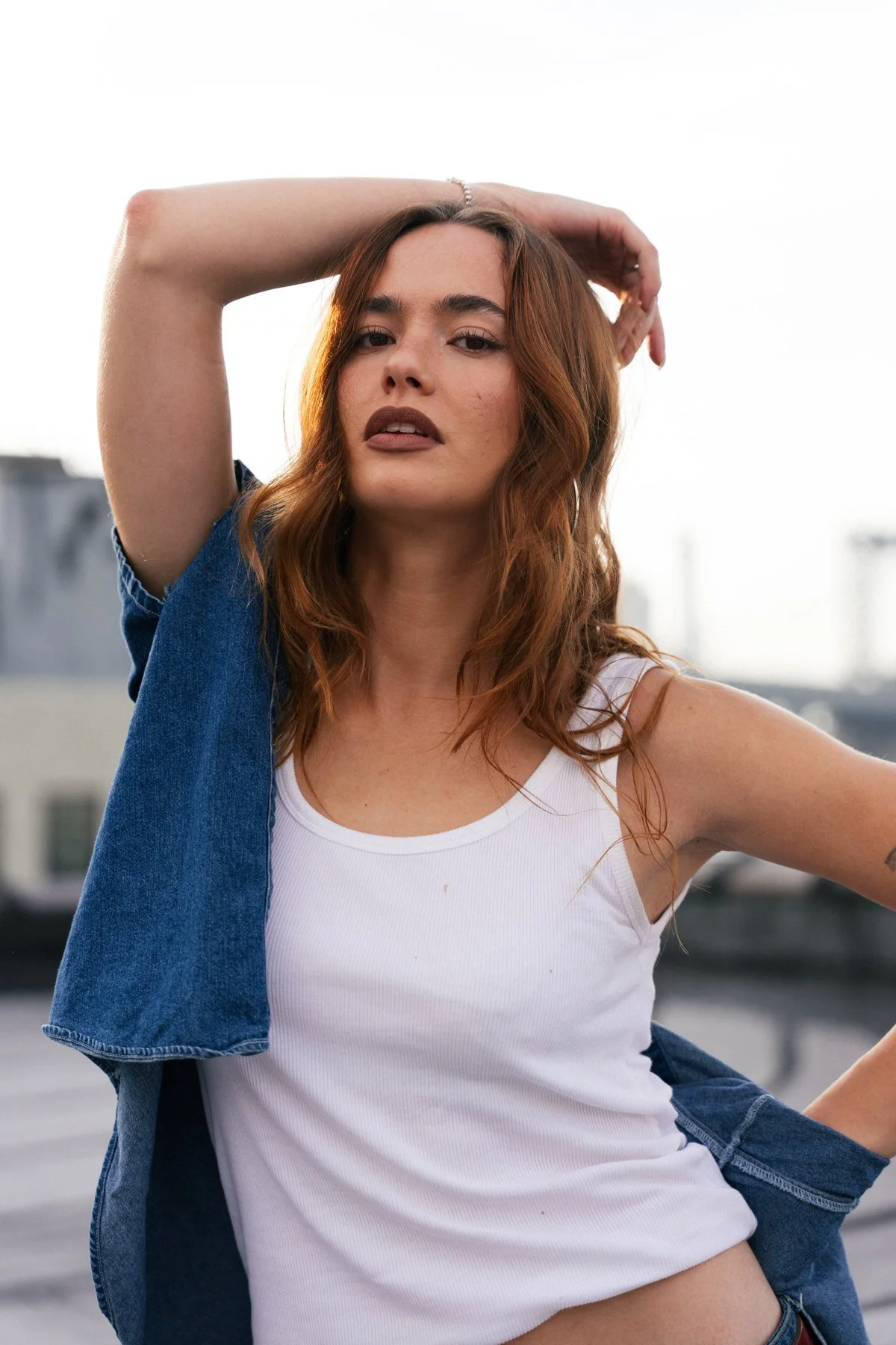Johnny in a white tank top with one arm raised on a rooftop