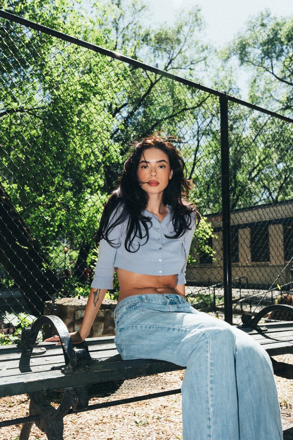 Hannahbeth seated beside a chain-link fence in a blue cardigan and jeans